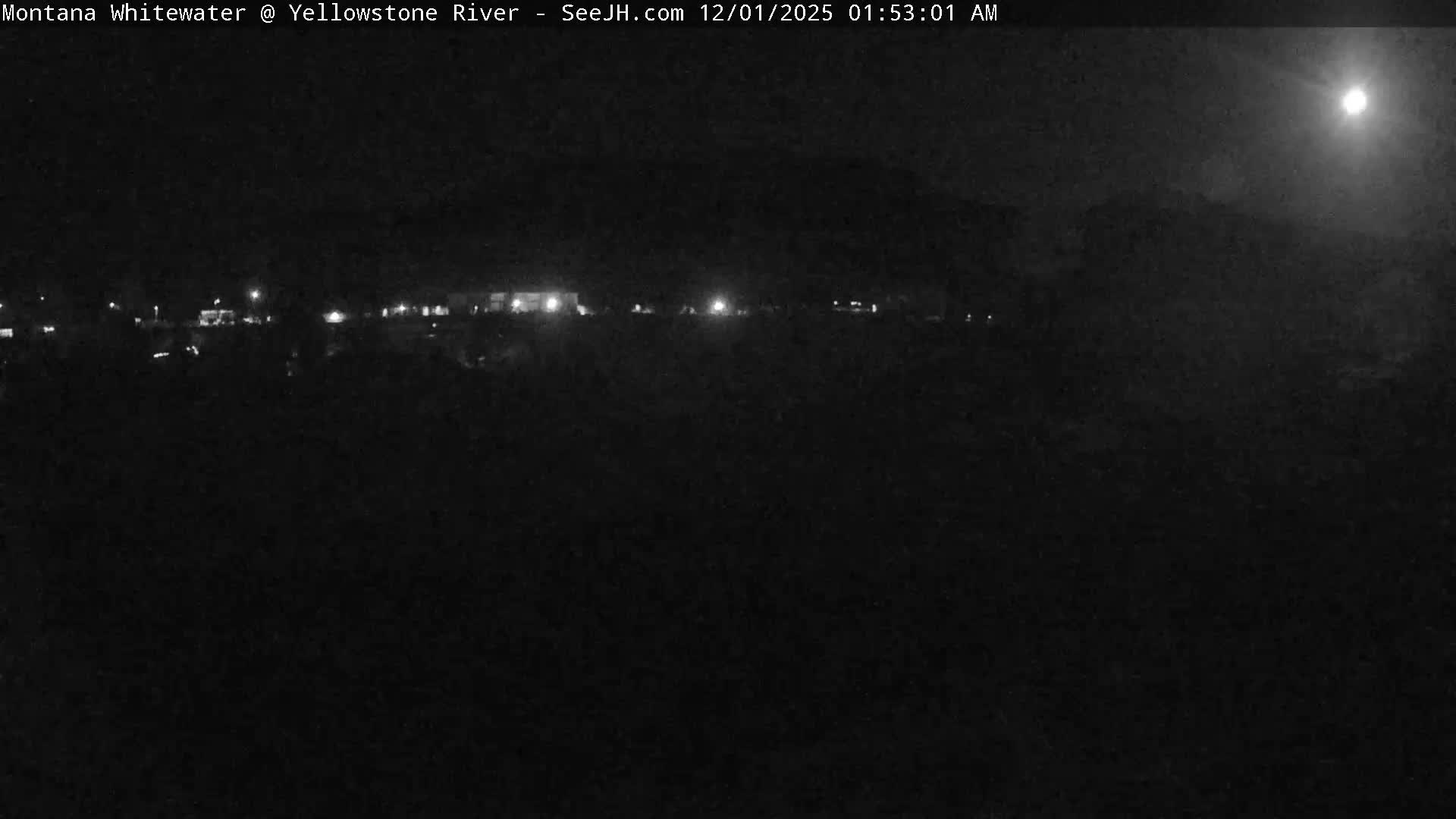 A dark, clear outdoor night scene features a bright moon in the upper right, with a horizontal line of scattered artificial lights visible across the midground against an otherwise indistinct, dark landscape.