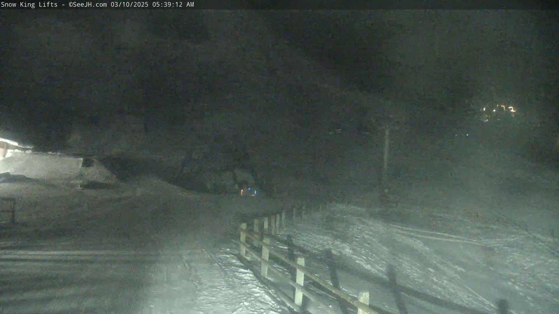 A snow-covered landscape is visible at night, with a wooden fence and faint lights in the distance.