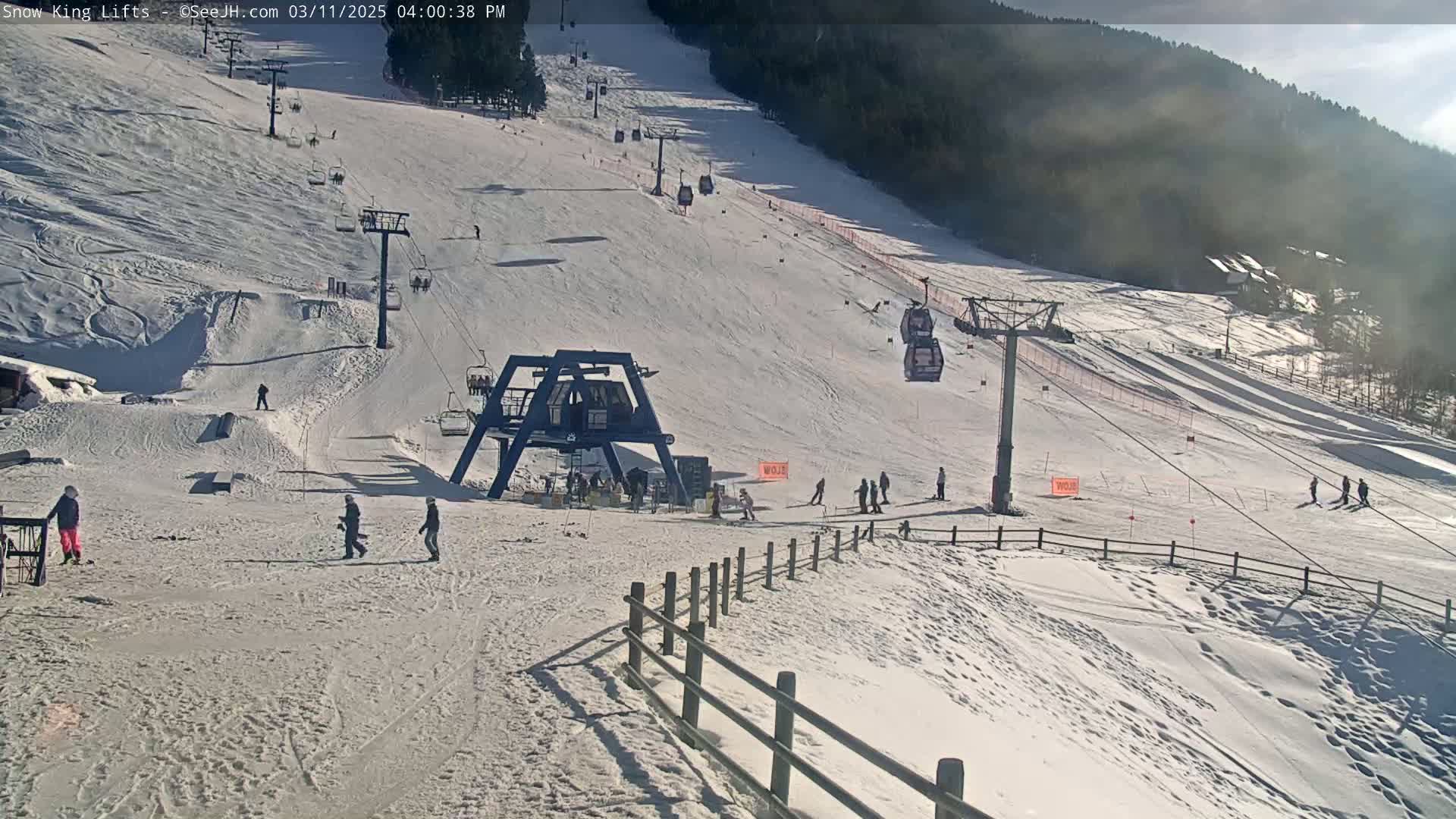 A sunny, snow-covered ski slope with several chairlifts and skiers visible on a partly cloudy day.