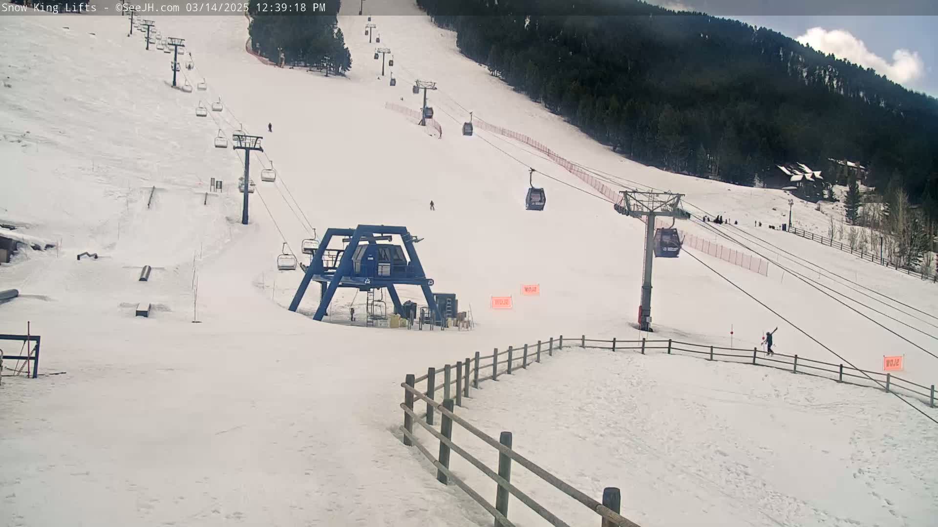 A mostly cloudy day at a snow-covered ski resort shows several chairlifts with skiers and snowboarders visible on the slopes.