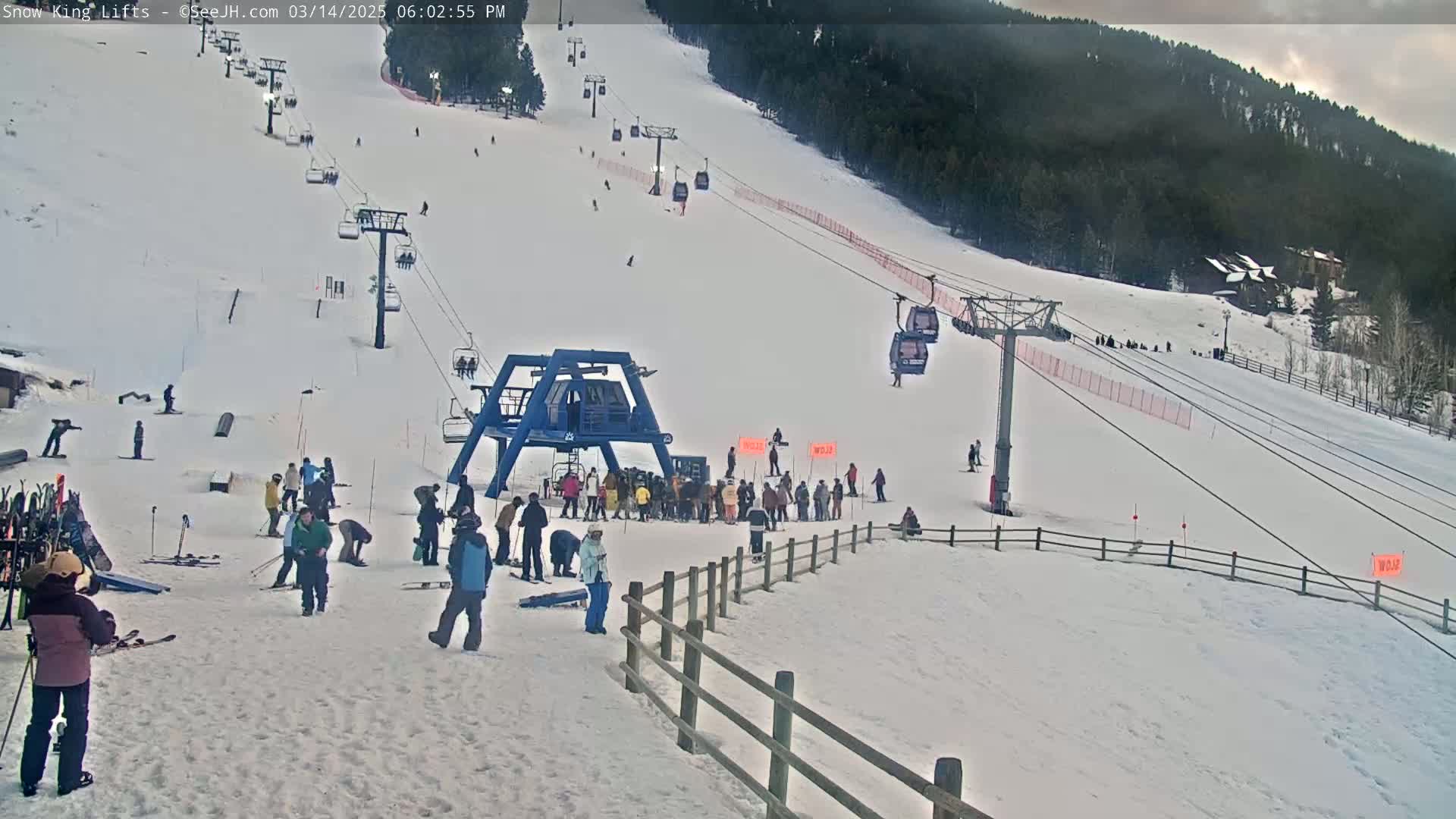 A ski slope with a chairlift and numerous skiers and snowboarders, under a partly cloudy sky.