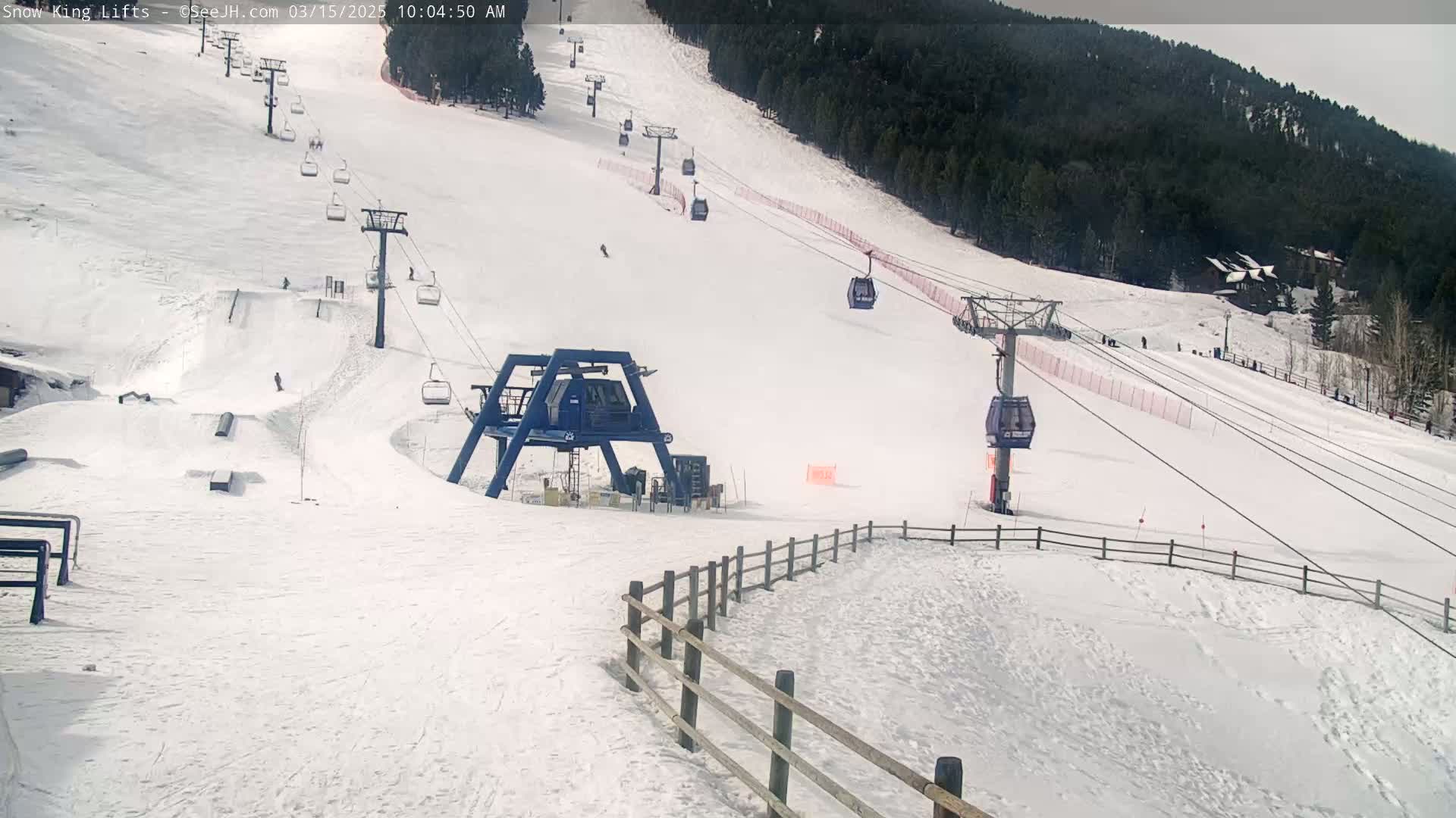 A snow-covered ski slope with several chairlifts and a few skiers visible on a partly sunny day.