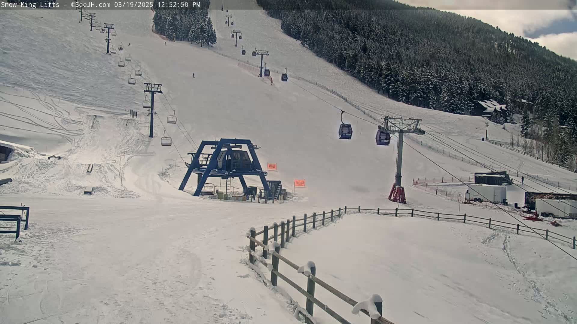 A snow-covered ski slope with several chairlifts and a base area, under cloudy skies.