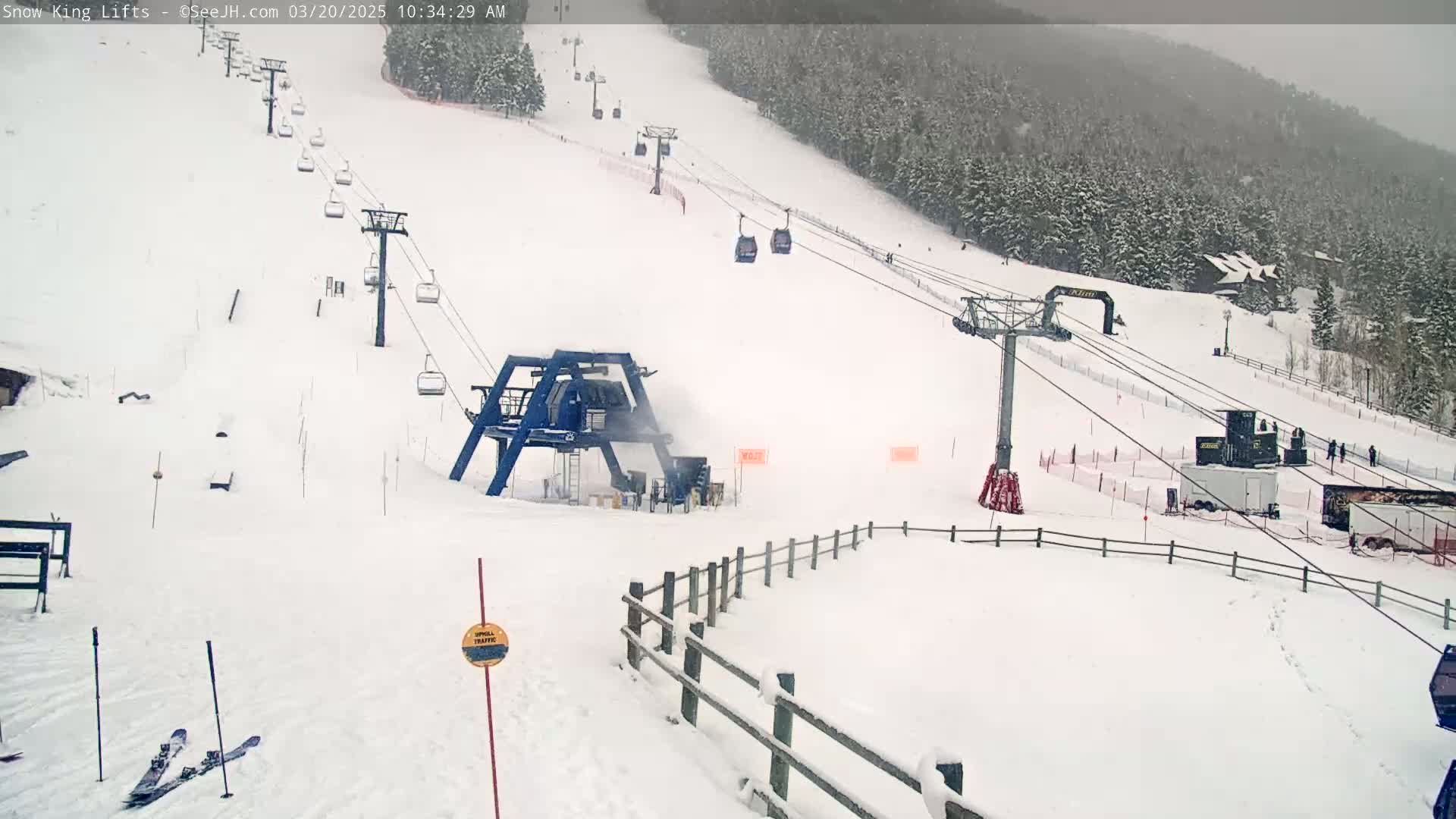 A snow-covered ski slope with several chairlifts and a snow-making machine operating under overcast skies.