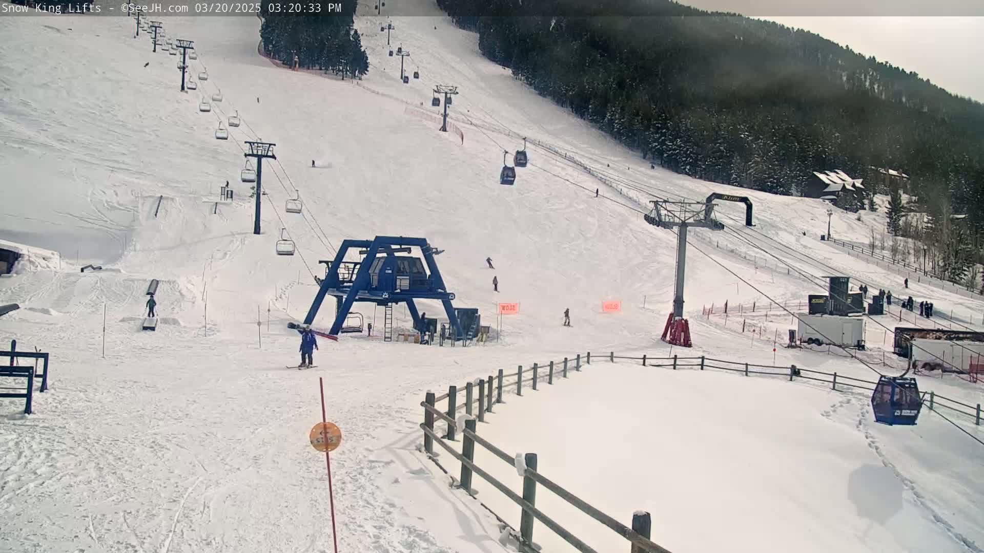 A snowy ski slope with several chairlifts, skiers, and a ski lift base station under a cloudy sky.