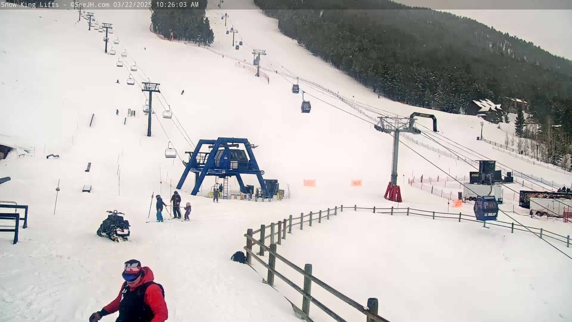 A snowy ski slope with several chairlifts and a few skiers and snowboarders visible on an overcast day.