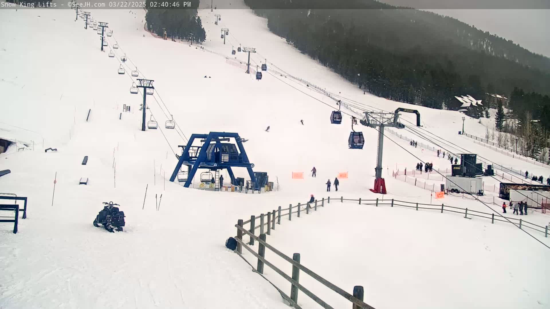 A snow-covered ski slope with several chairlifts, skiers, and snowboarders under an overcast sky.