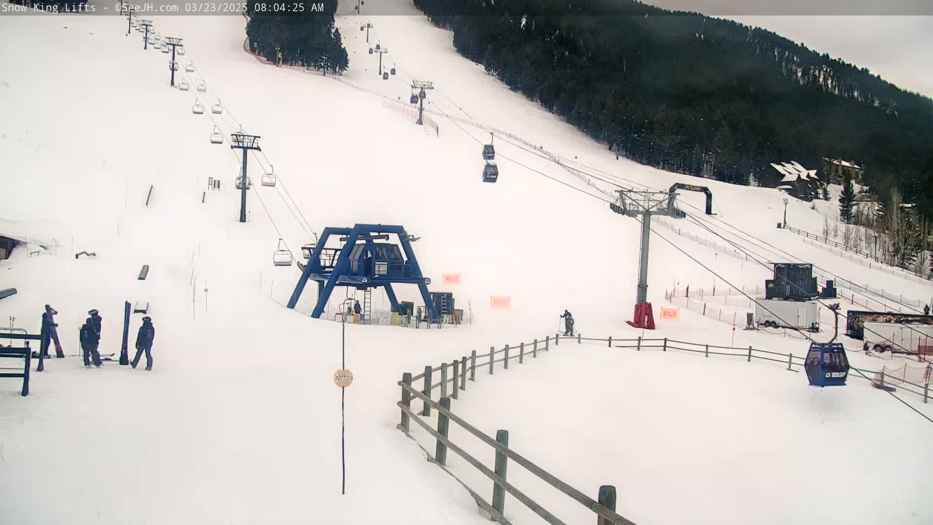 A snow-covered ski slope with several chairlifts and a few skiers visible under an overcast sky.
