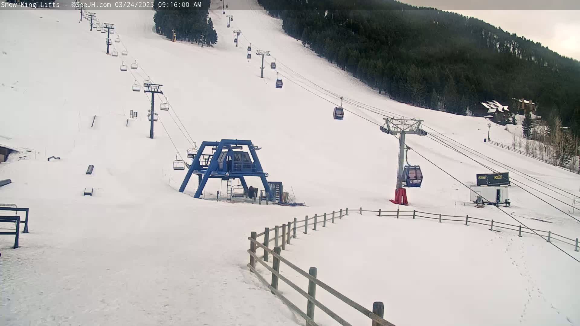 A snow-covered ski slope with several chairlifts and a base station, under an overcast sky.