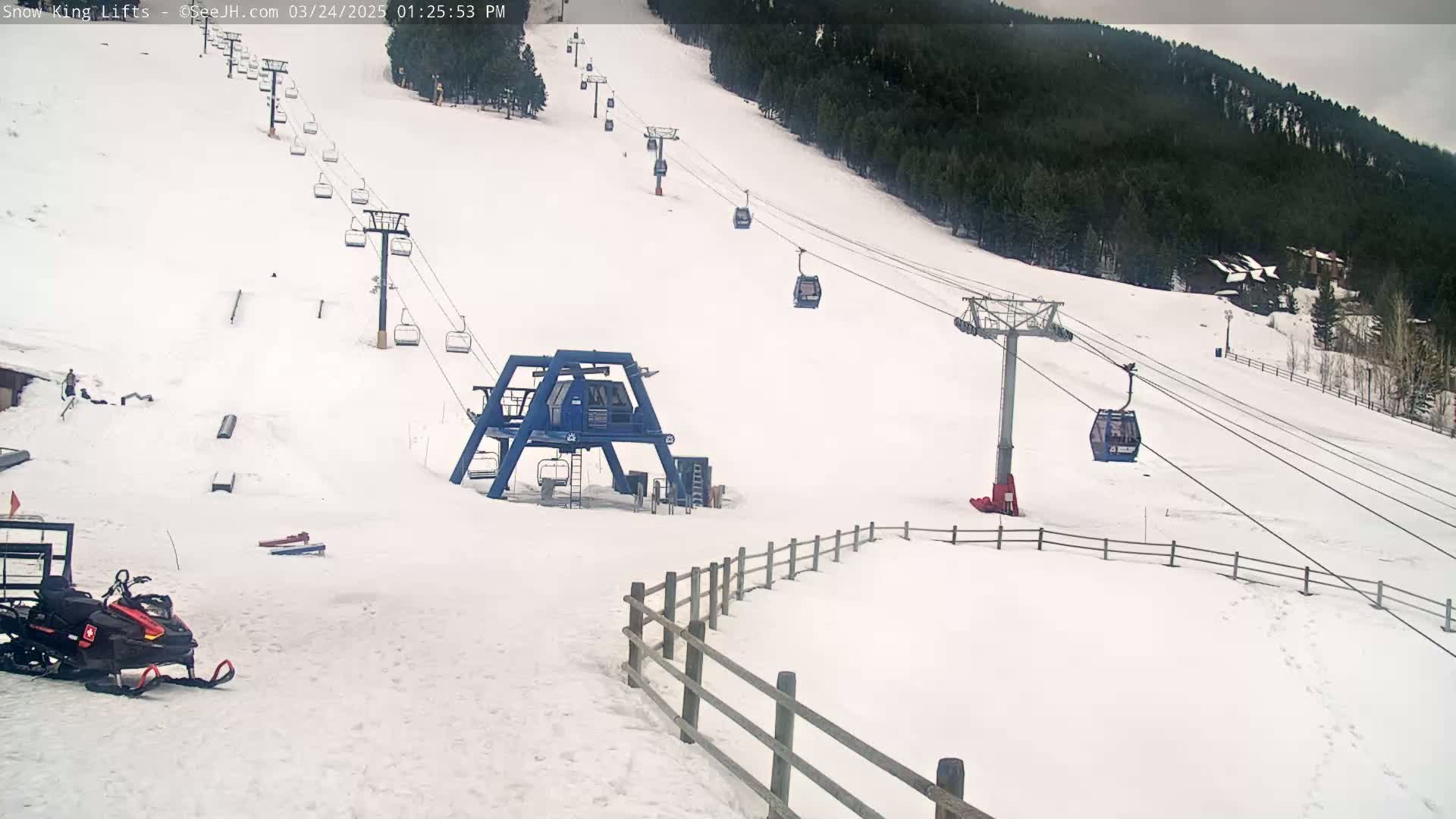 A snow-covered ski slope with several chairlifts and a snowmobile parked at the bottom, under an overcast sky.