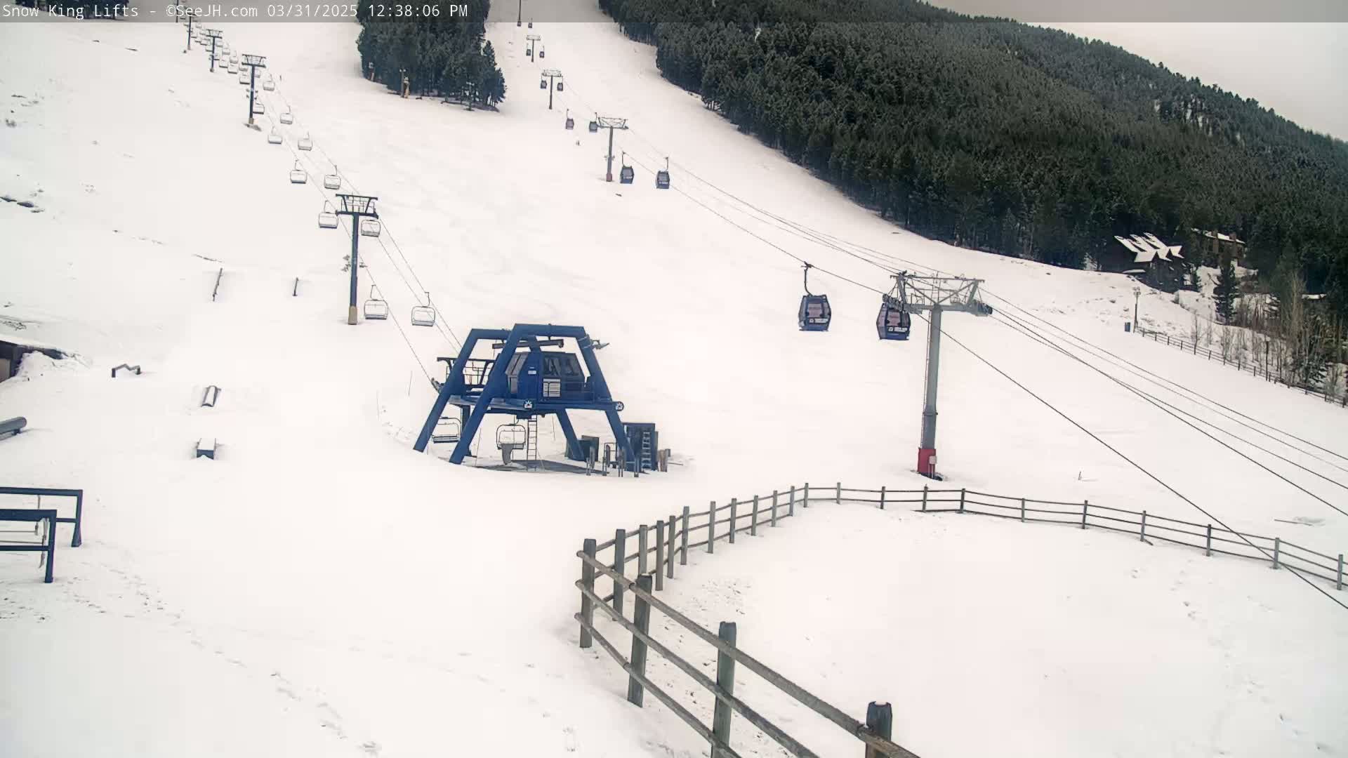 A snow-covered ski slope with several chairlifts and a wooden fence in the foreground, under an overcast sky.