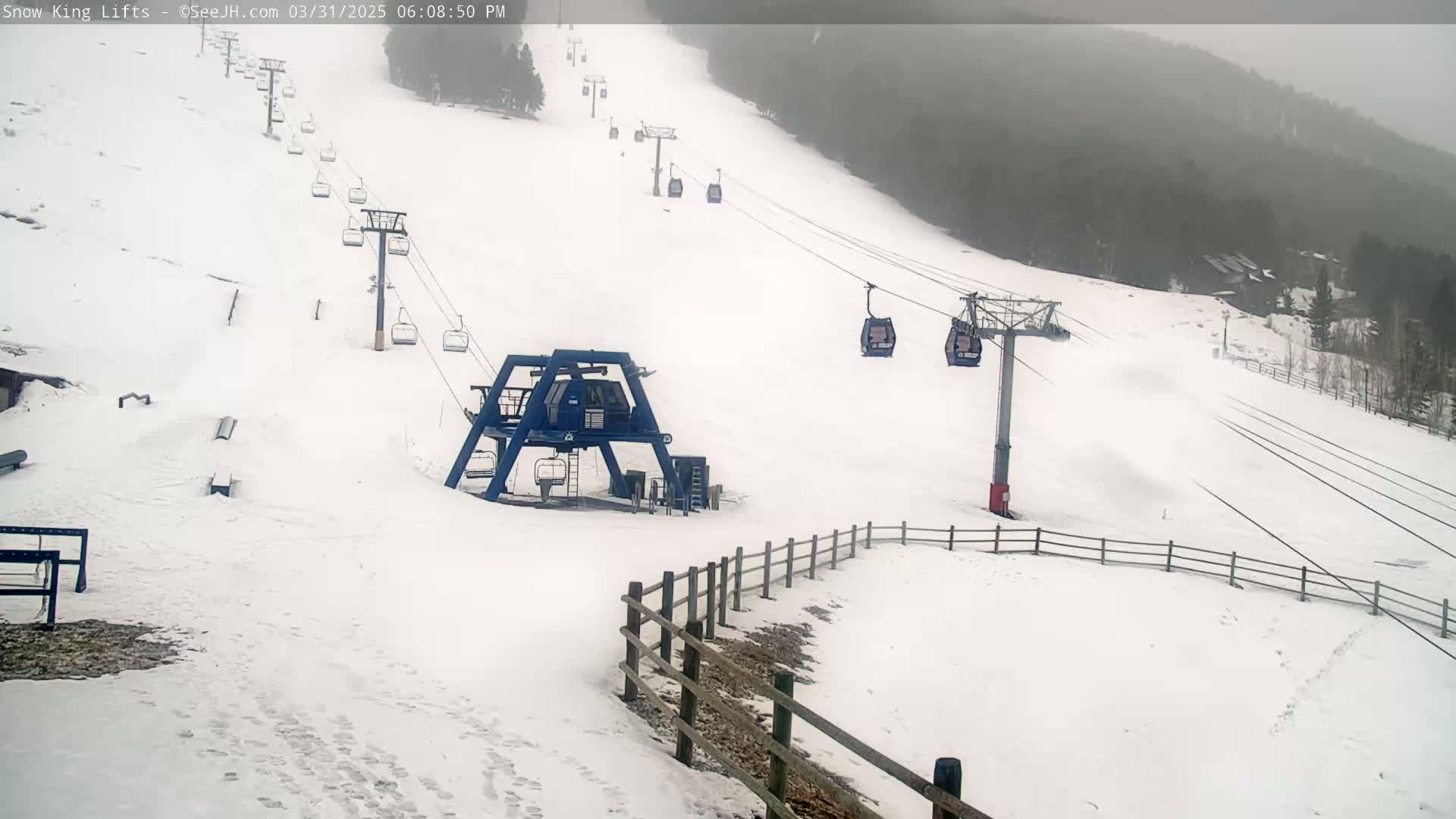 A snow-covered ski slope with several chairlifts and a lift station, under overcast skies.