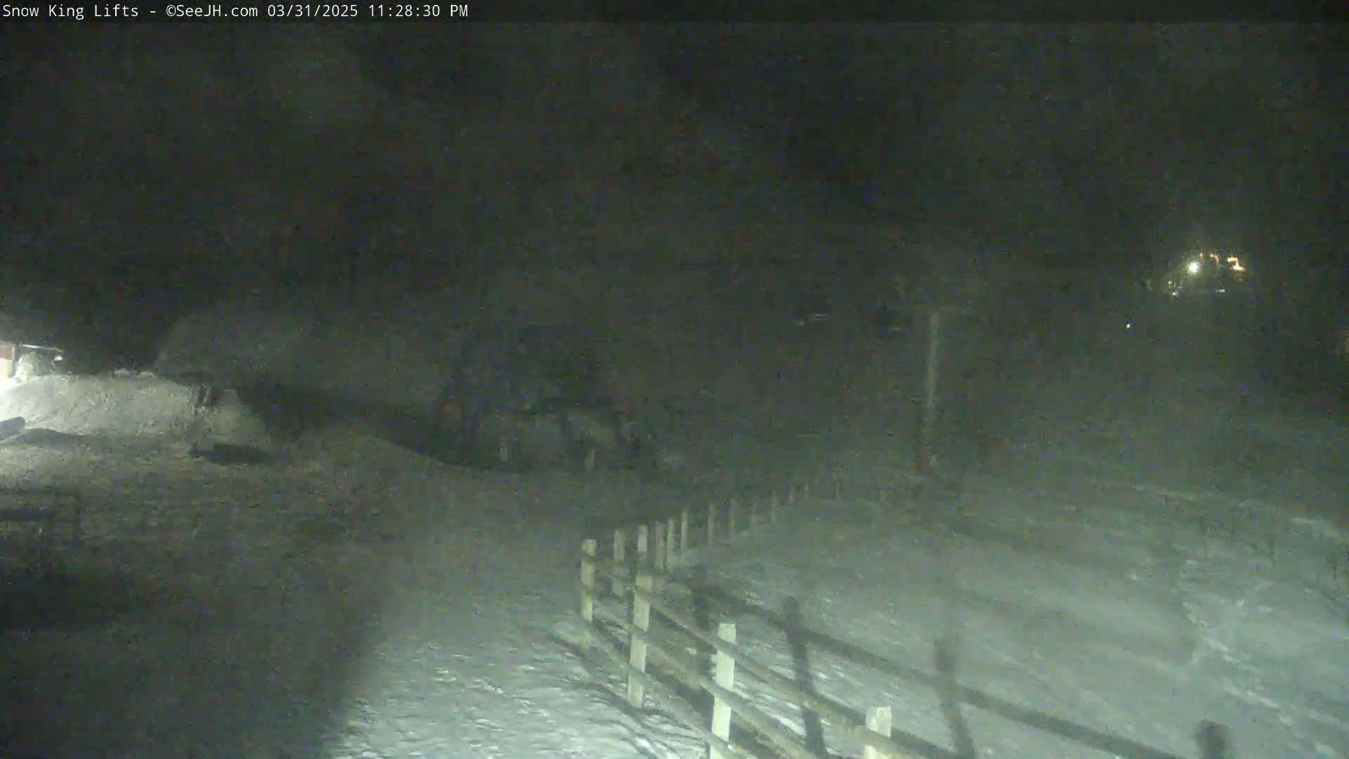 A snow-covered area at night is partially visible, showing a wooden fence and indistinct objects in the distance under dark conditions.