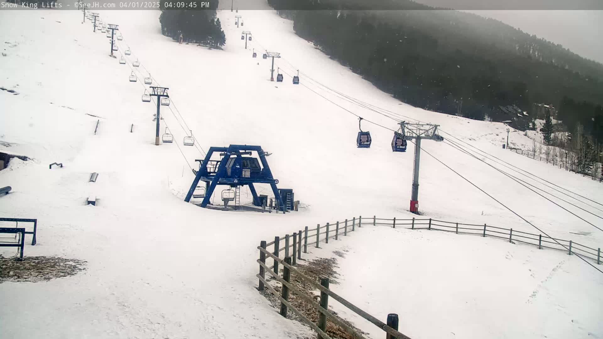 A snow-covered ski slope with several chairlifts and a base station, under lightly snowing conditions.