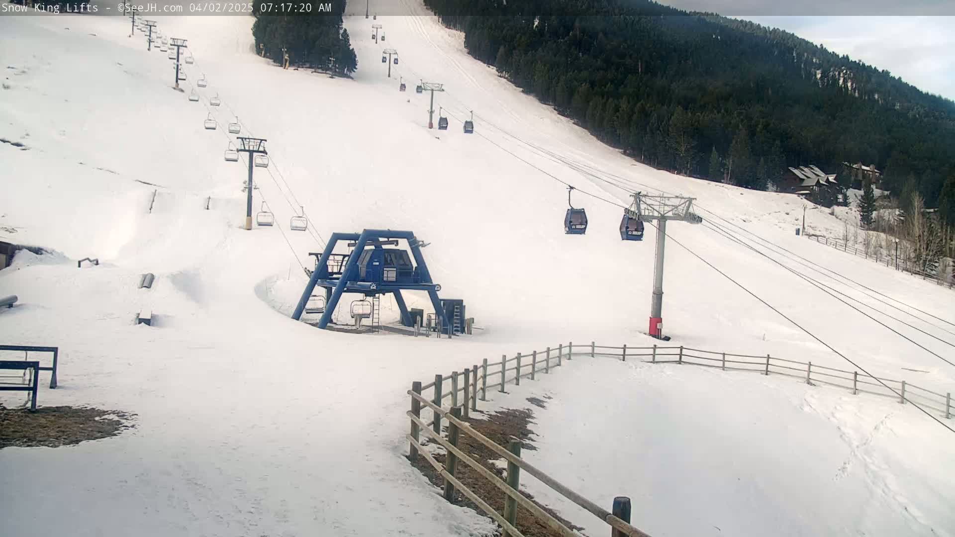 A snow-covered ski slope with several chairlifts and gondolas, under a cloudy sky.