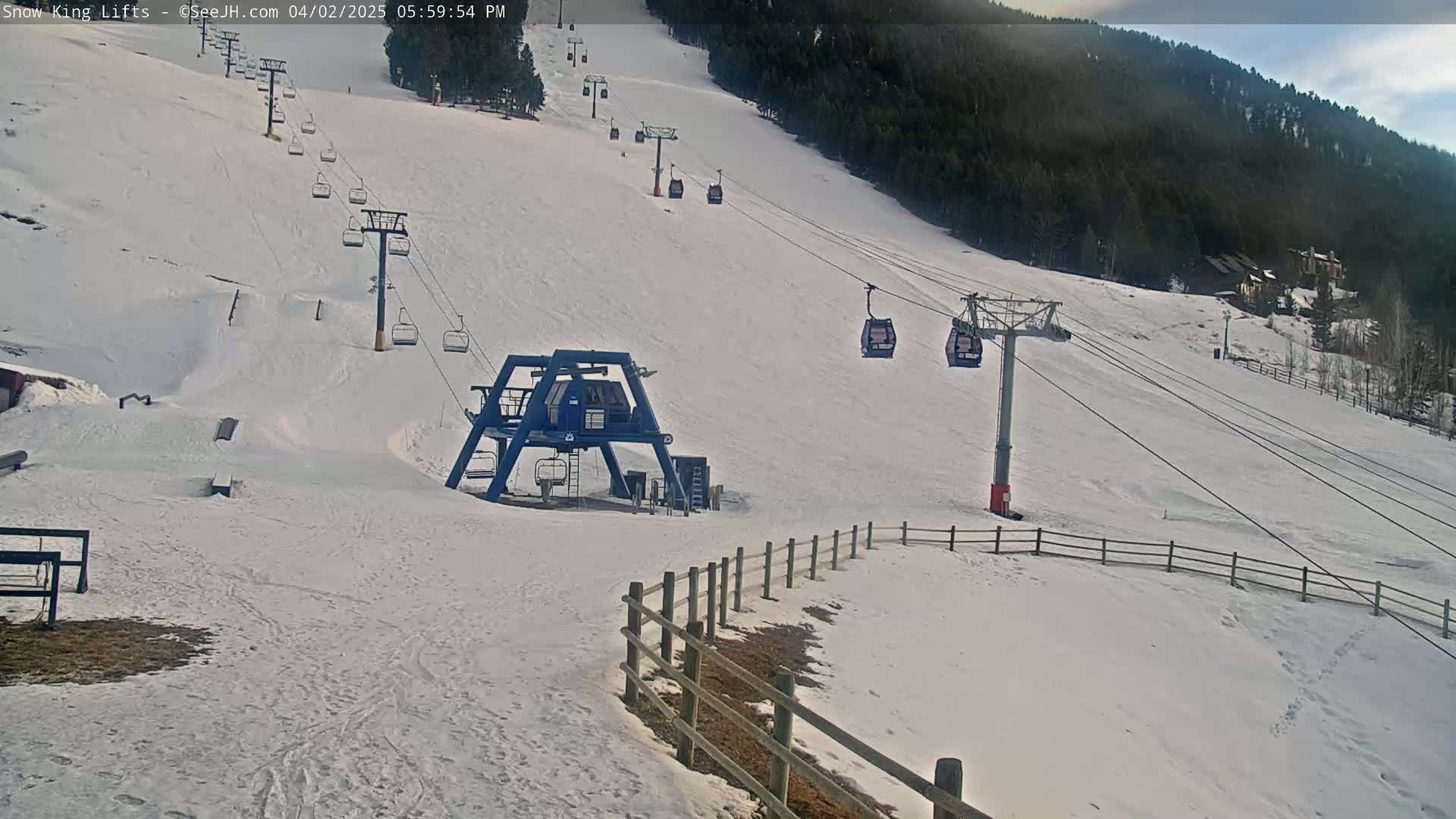 A snow-covered ski slope with several chairlifts and a base station under a partly cloudy sky.
