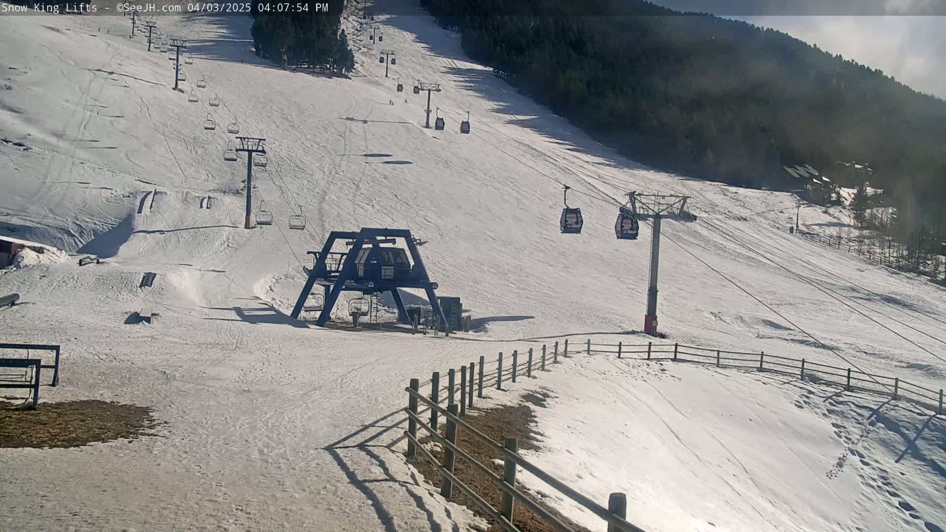 A snow-covered ski slope with several chairlifts and a ski lift base station under mostly sunny skies.