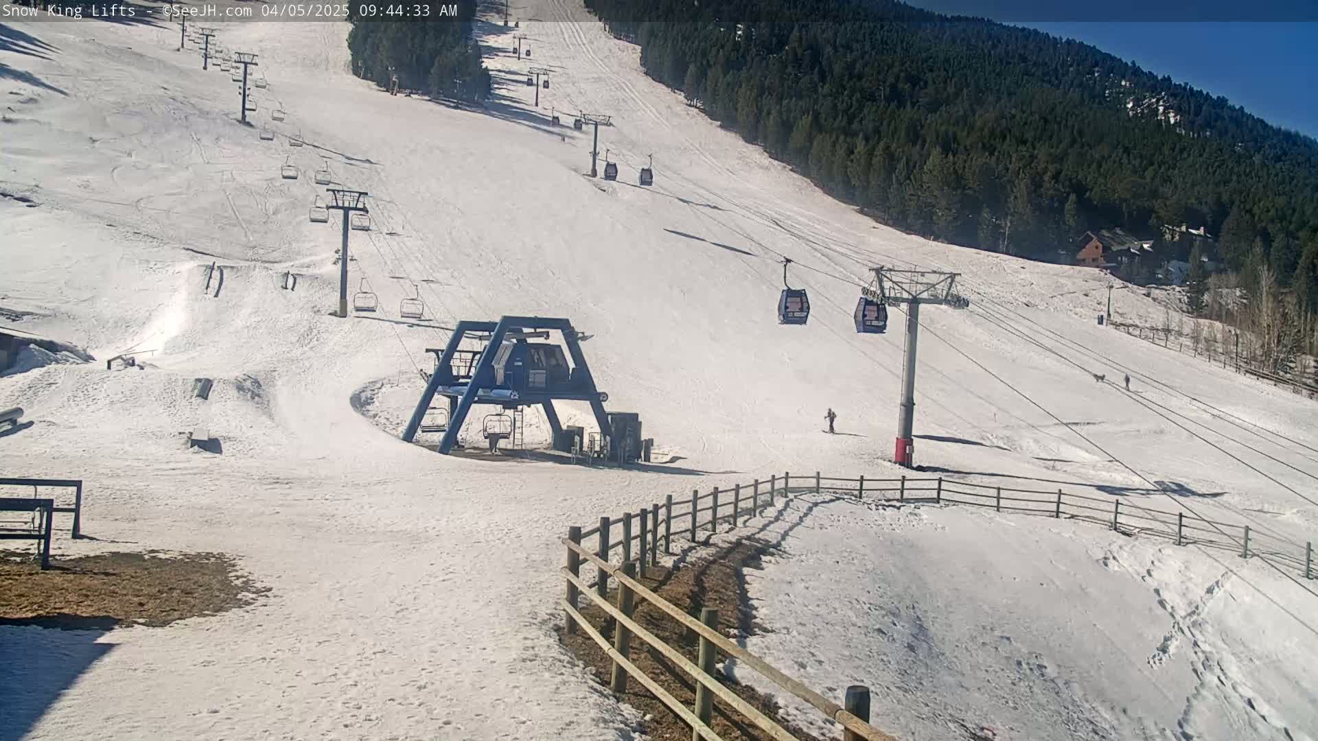 A snow-covered ski slope with several chairlifts and a few skiers visible on a sunny day.