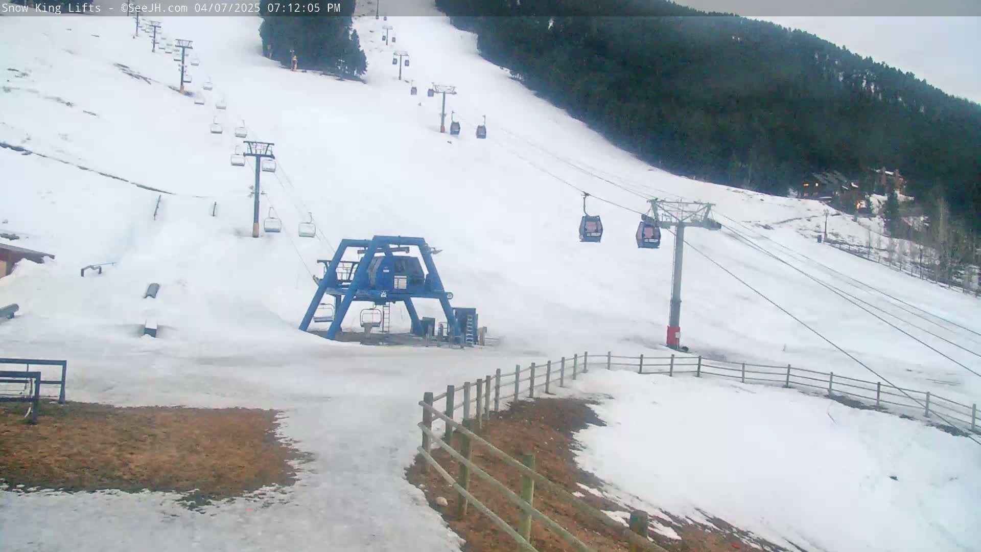A snow-covered ski slope with several chairlifts and a ski lift base station under an overcast sky.