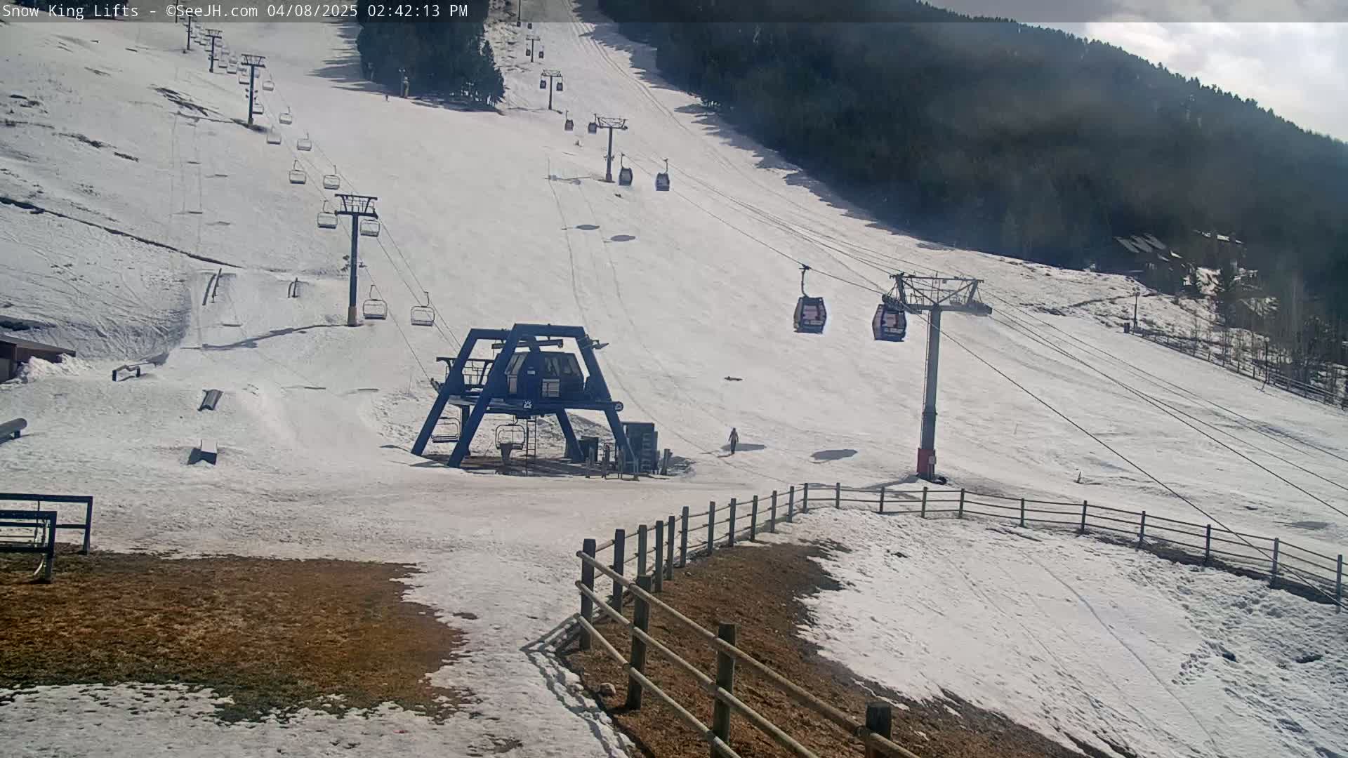 A snow-covered ski slope with several chairlifts and a few people visible on a partly cloudy day.