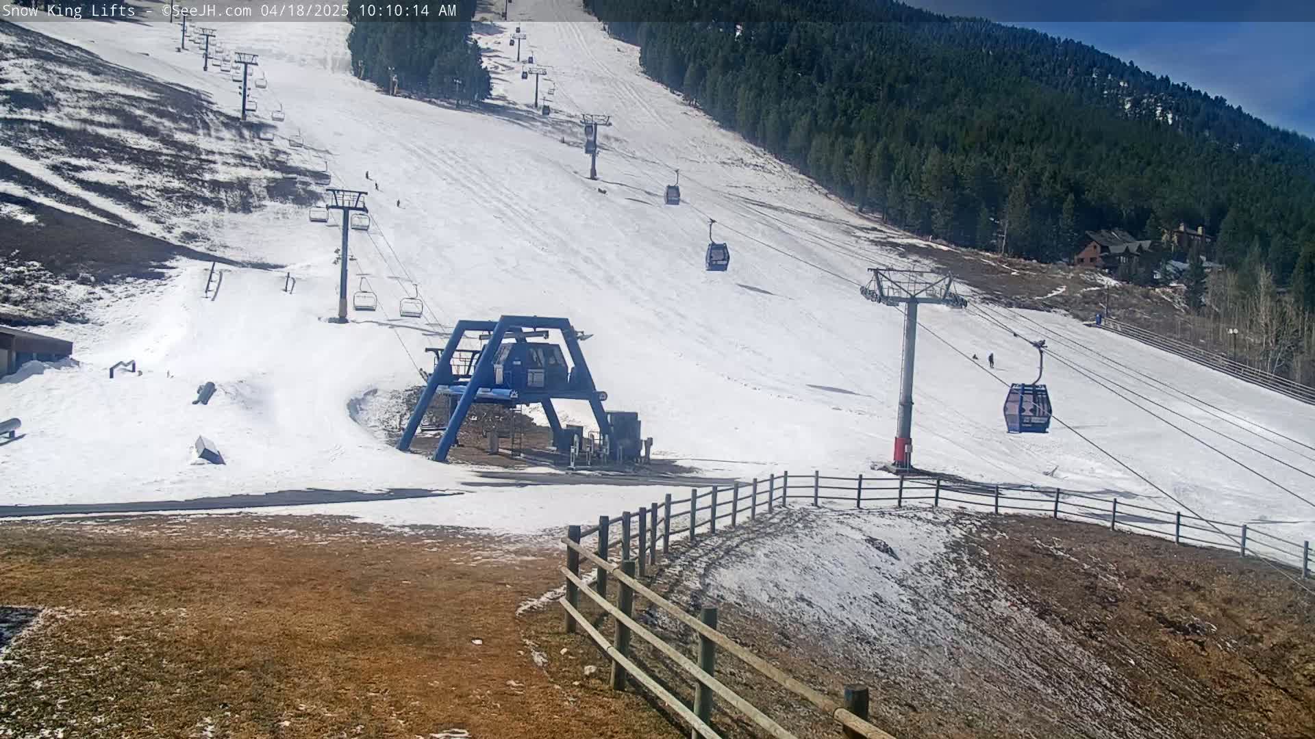 A ski slope with several chairlifts and sparsely populated runs under a sunny sky.