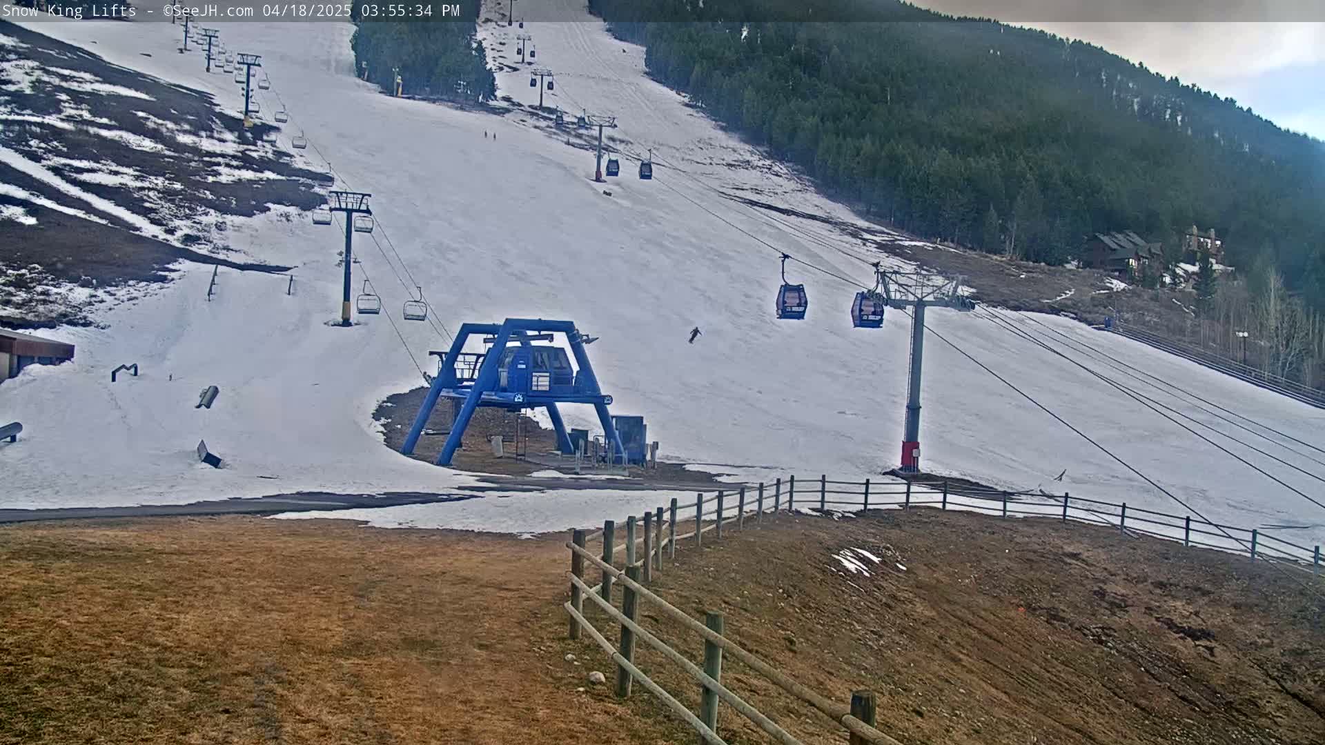 A ski lift with several empty chairs ascends a snow-covered hill under an overcast sky.