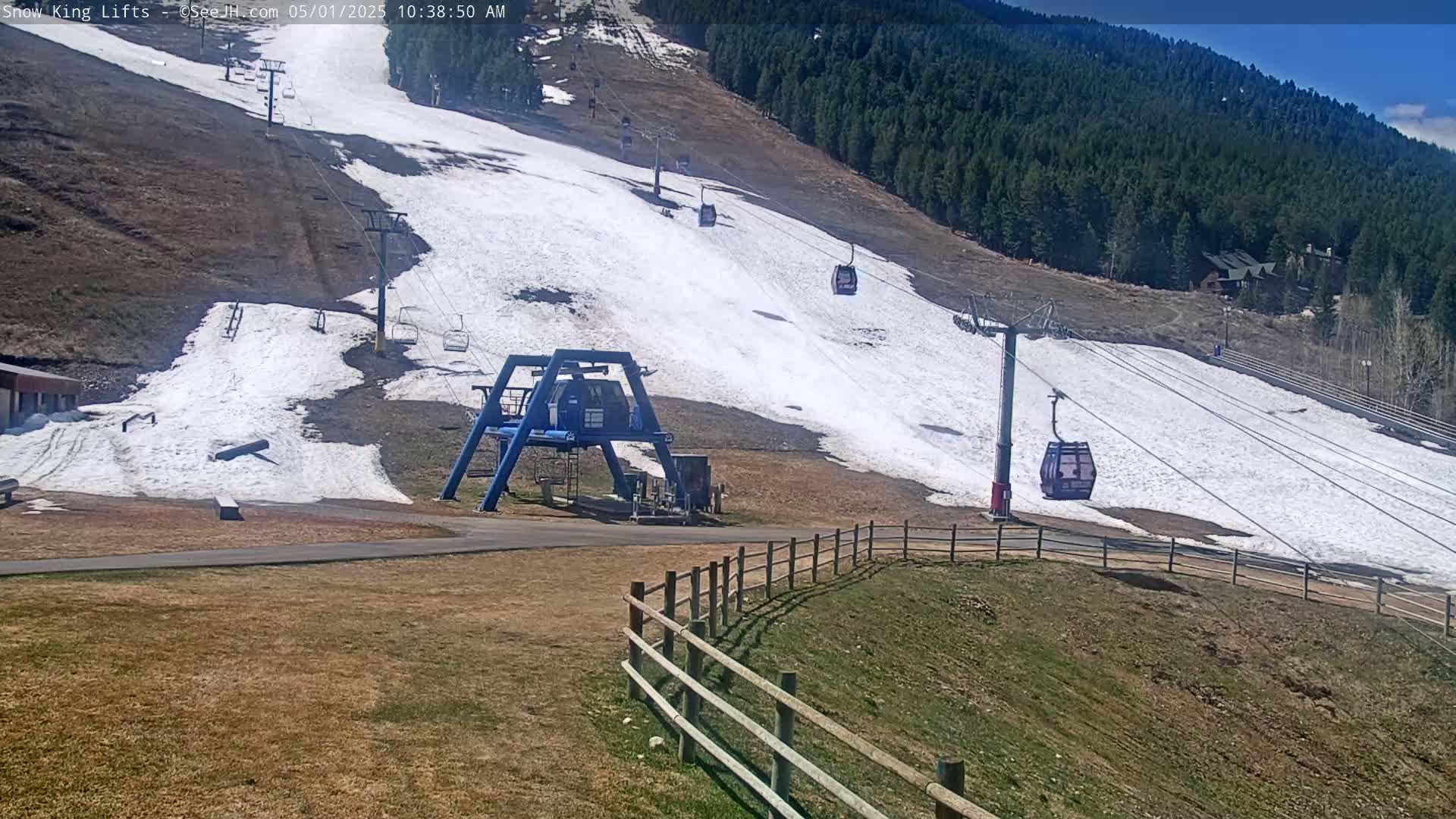 A ski lift with several gondolas ascends a hill partially covered in snow, under a clear sky.