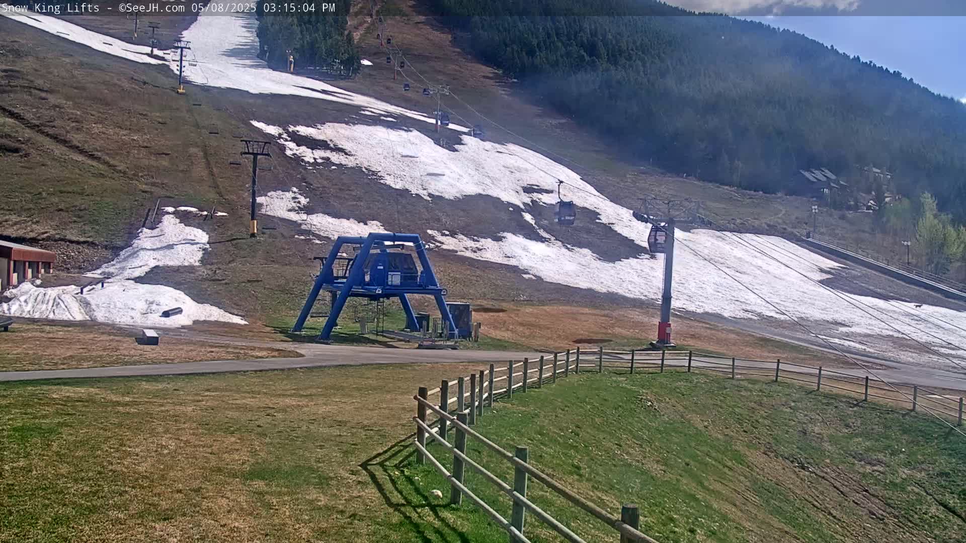 A ski lift and chairlifts are visible on a mostly brown hill with patches of melting snow under a partly sunny sky.