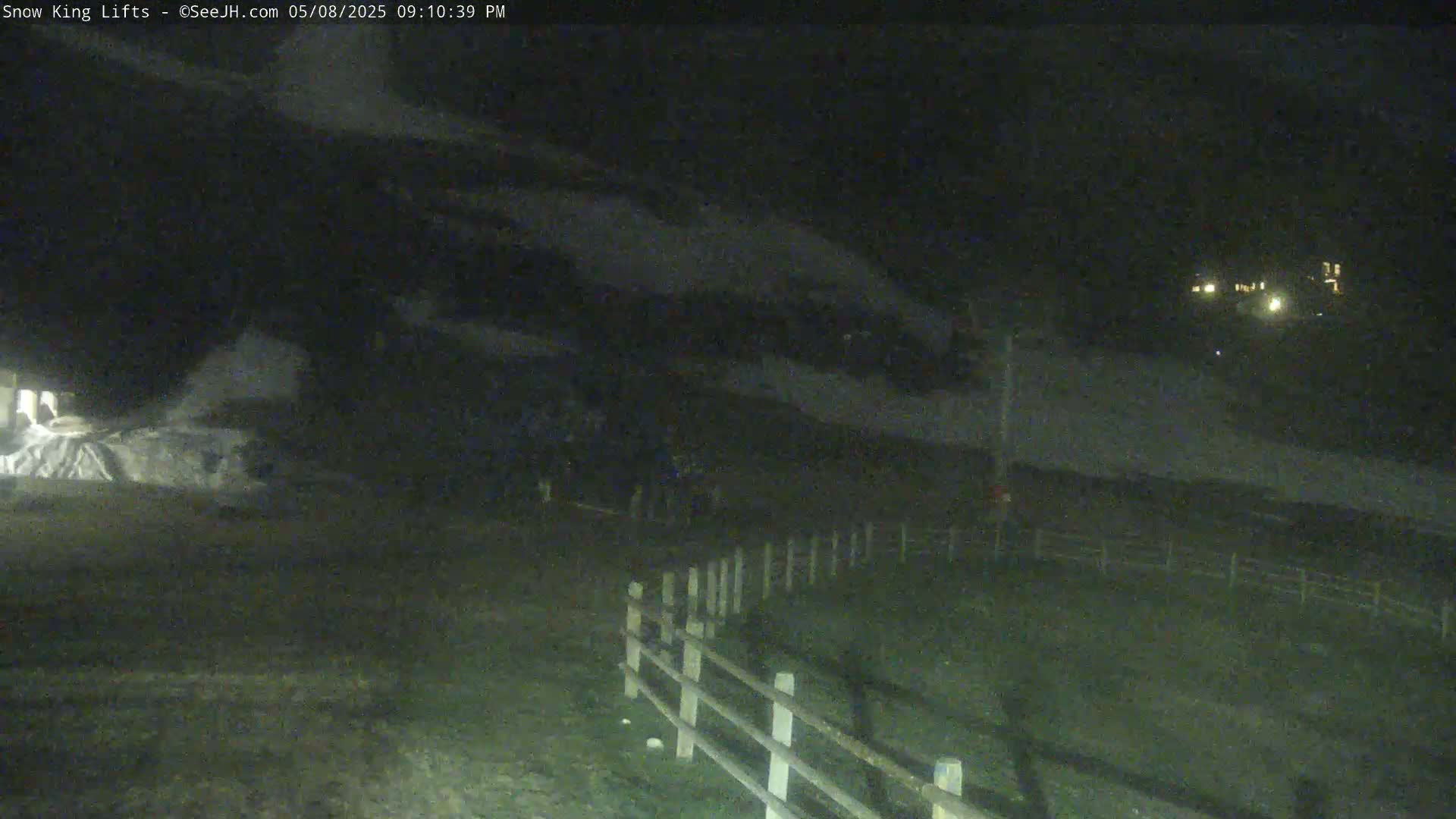 A nighttime, snow-covered landscape is visible, featuring a wooden fence and a few distant lights.