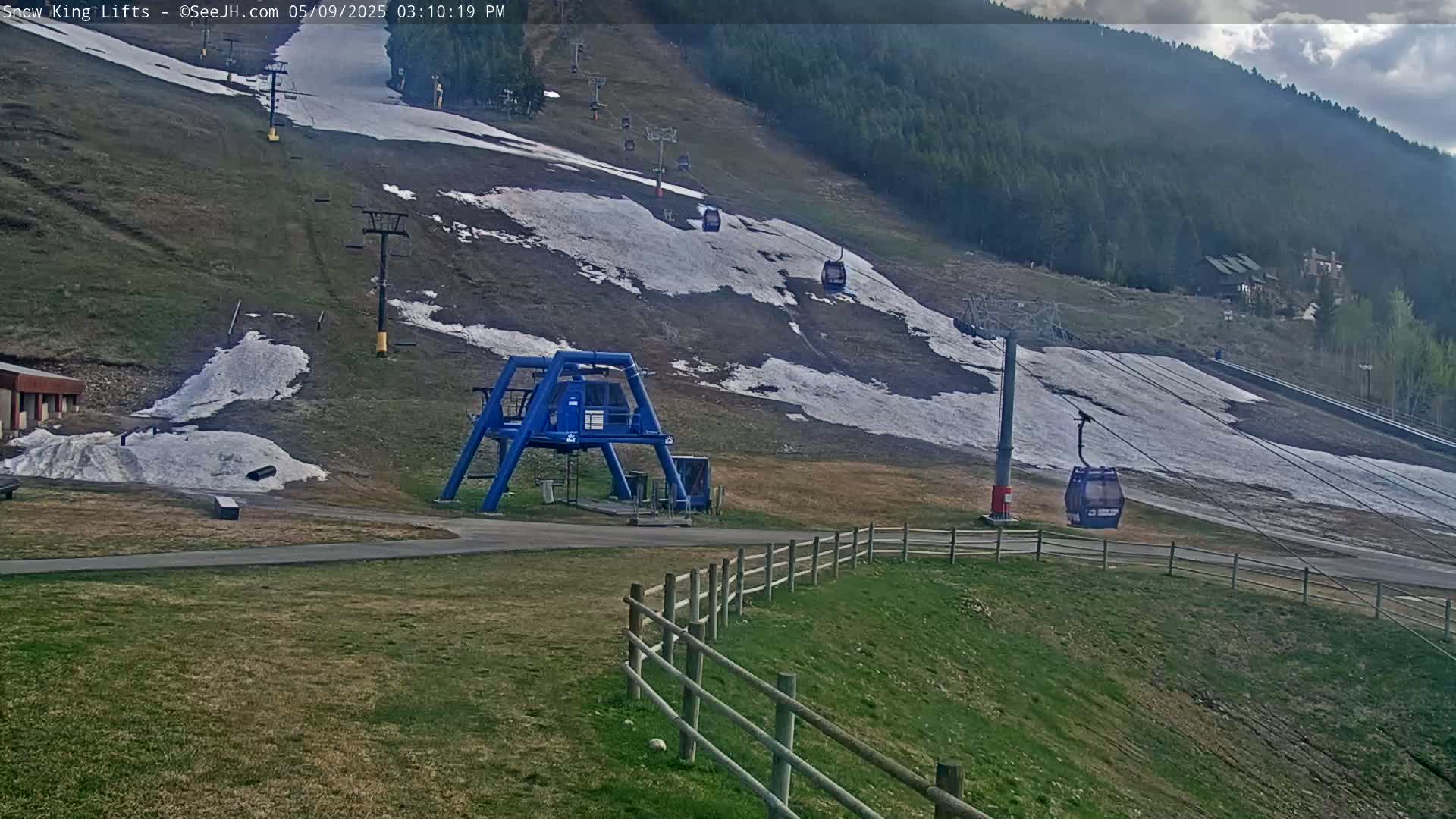 A ski lift with partially melted snow on the slopes, under partly cloudy skies.