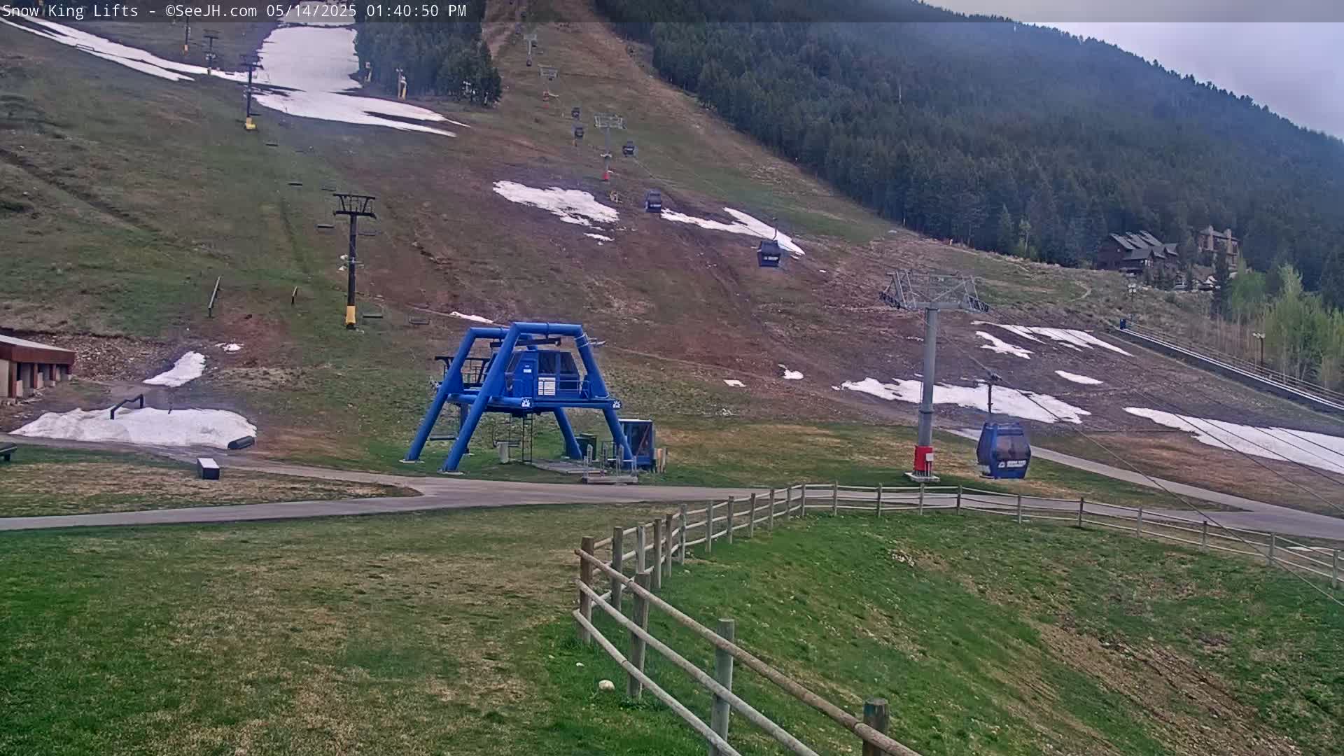 A ski lift and several chairlifts are visible on a mostly brown hill with patches of snow, under an overcast sky.