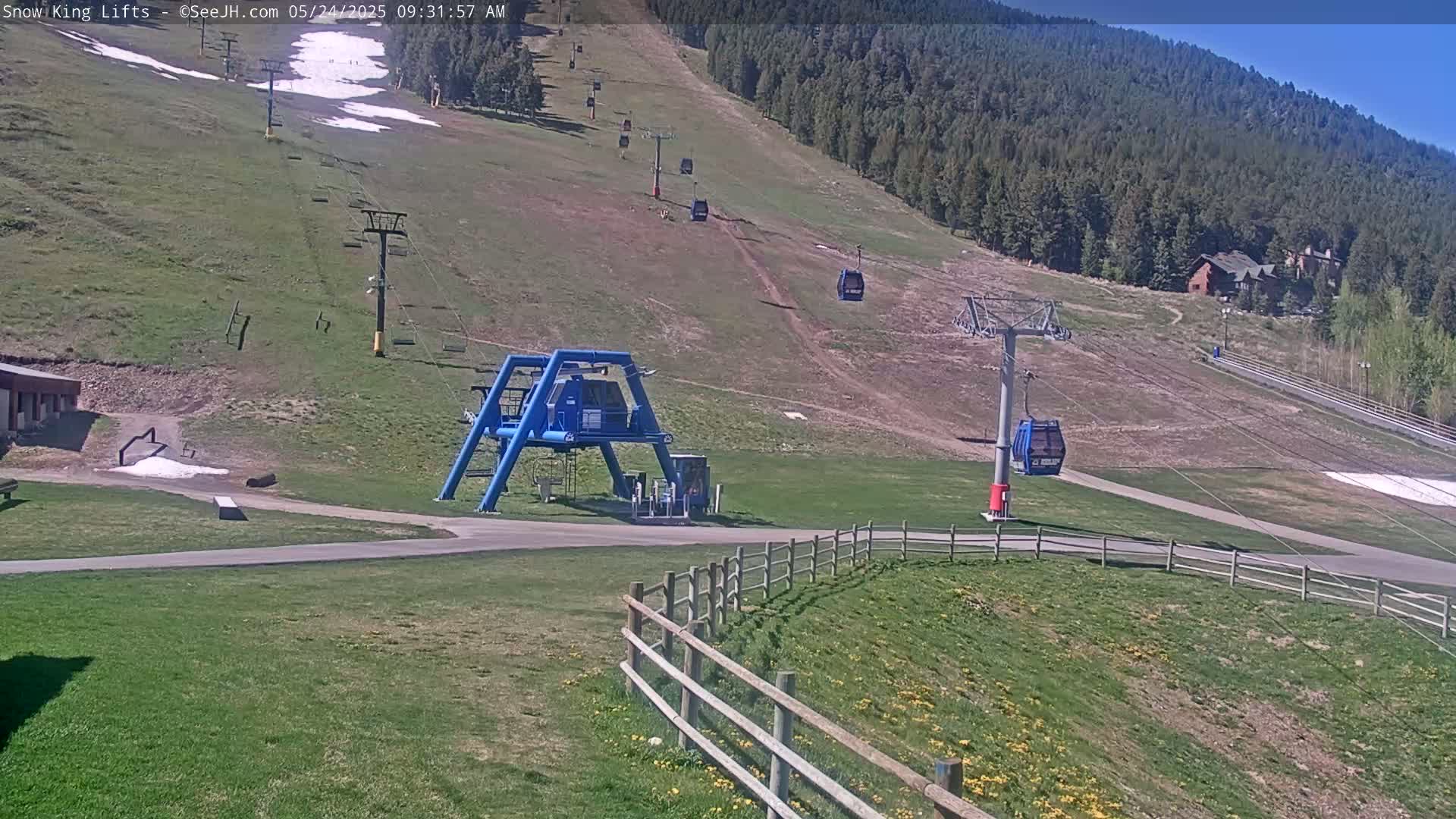 A grassy ski lift area with several empty blue chairlifts, under a mostly sunny sky.