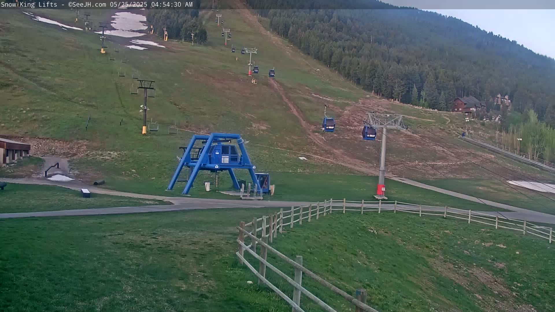 A ski lift base station and several chairlifts ascend a grassy hill under a partly cloudy sky.