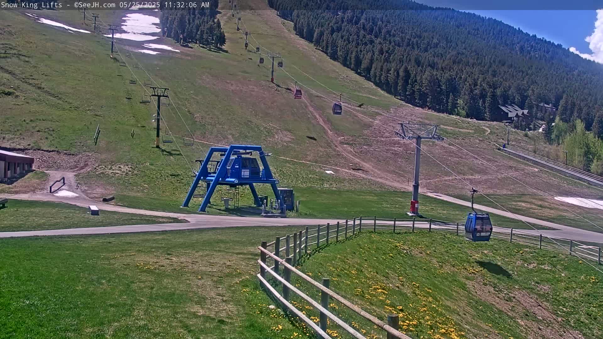 A ski lift base station with several chairlifts ascending a grassy mountainside under a sunny sky.