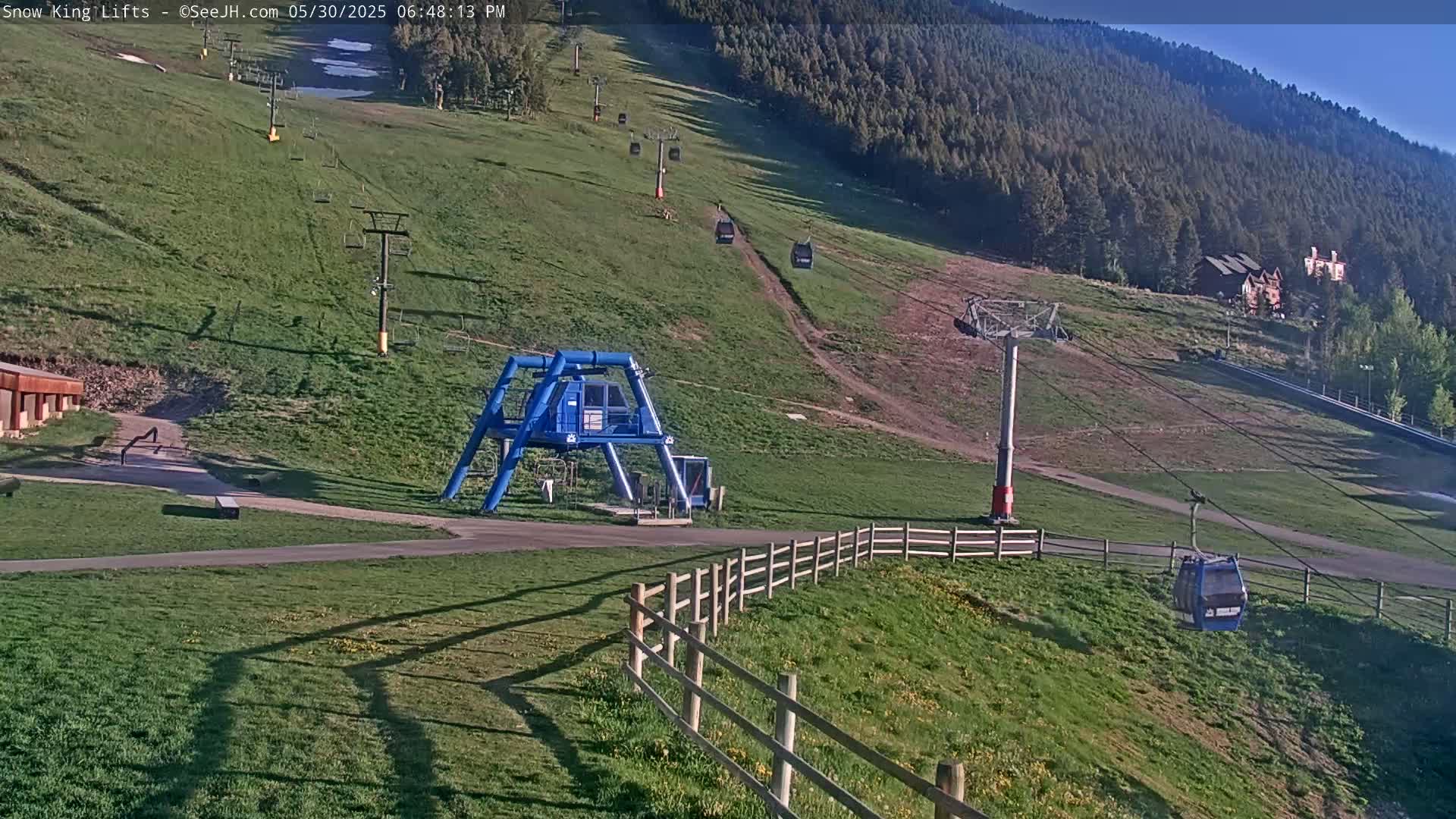A ski lift base station and several chairlifts ascending a grassy hillside under a clear, sunny sky.