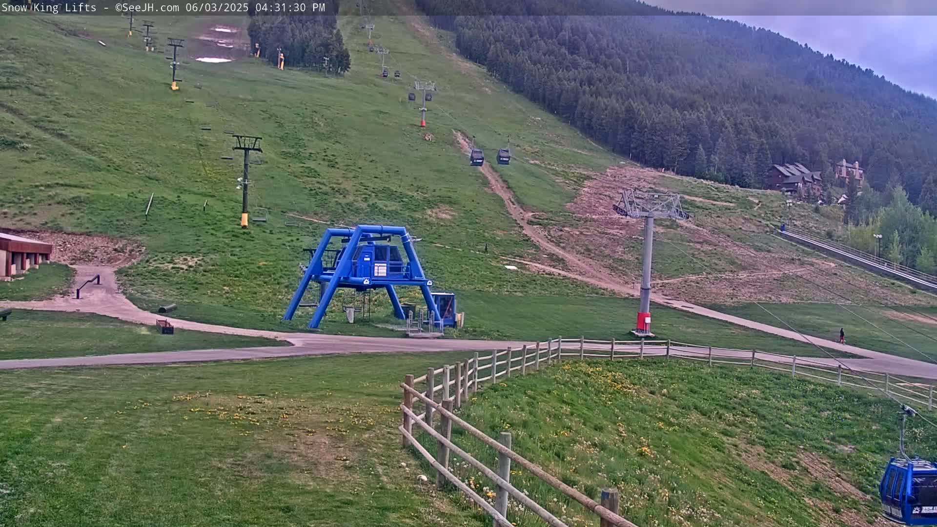 A ski lift base area with several chairlifts ascending a grassy hillside under an overcast sky.