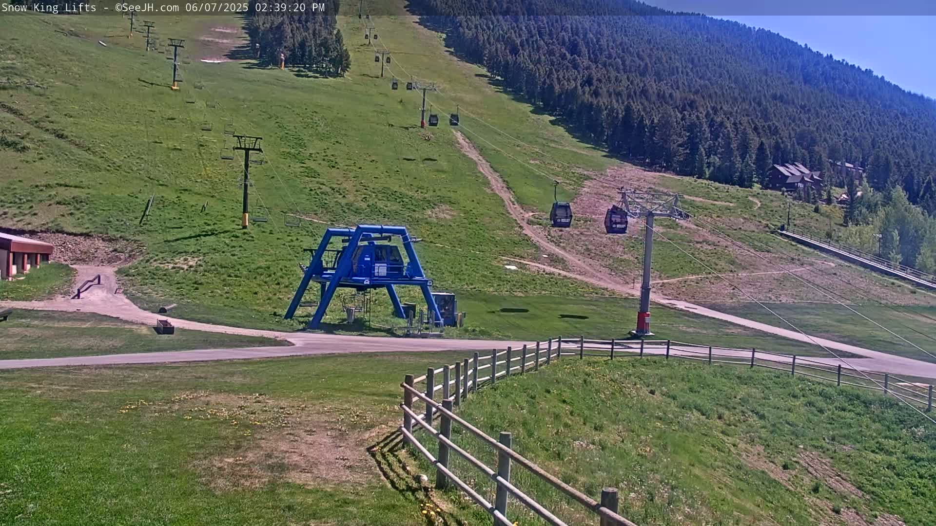 A ski lift base station with several chairlifts ascending a grassy mountainside under a clear, sunny sky.