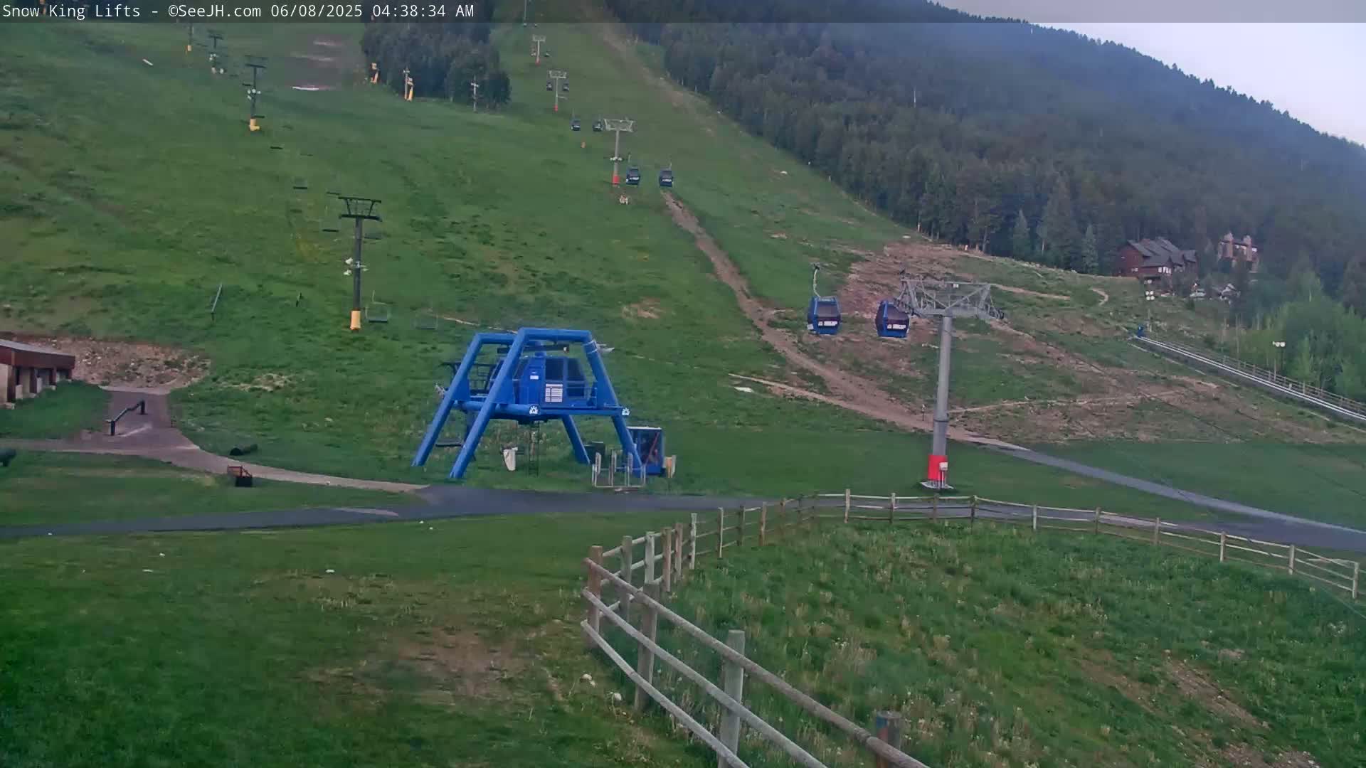 A grassy hillside with several chairlifts and a gondola, under an overcast sky.