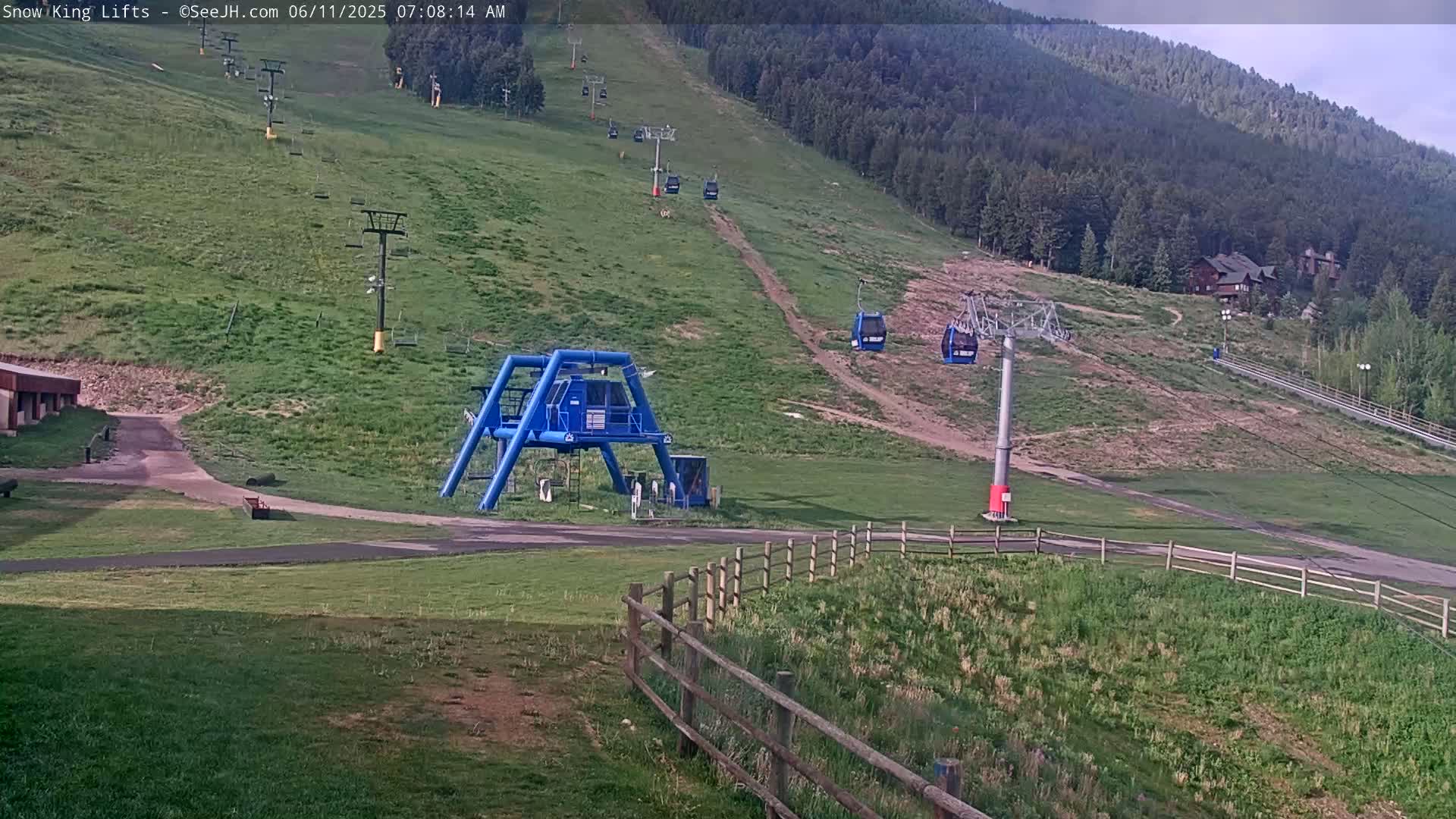 A grassy hillside with several empty chairlifts and a ski lift base station under a partly cloudy sky.