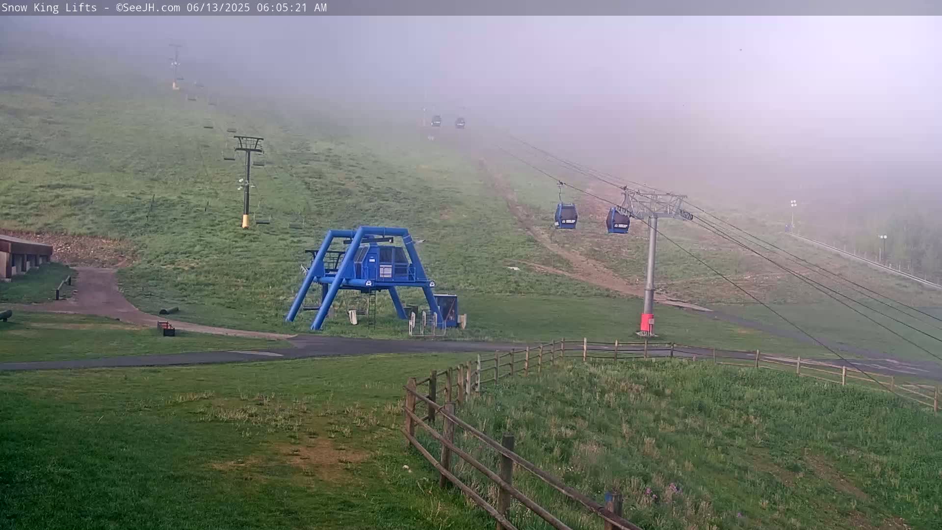 A fog-shrouded grassy hill shows several chairlifts ascending, with a blue lift station at the bottom.