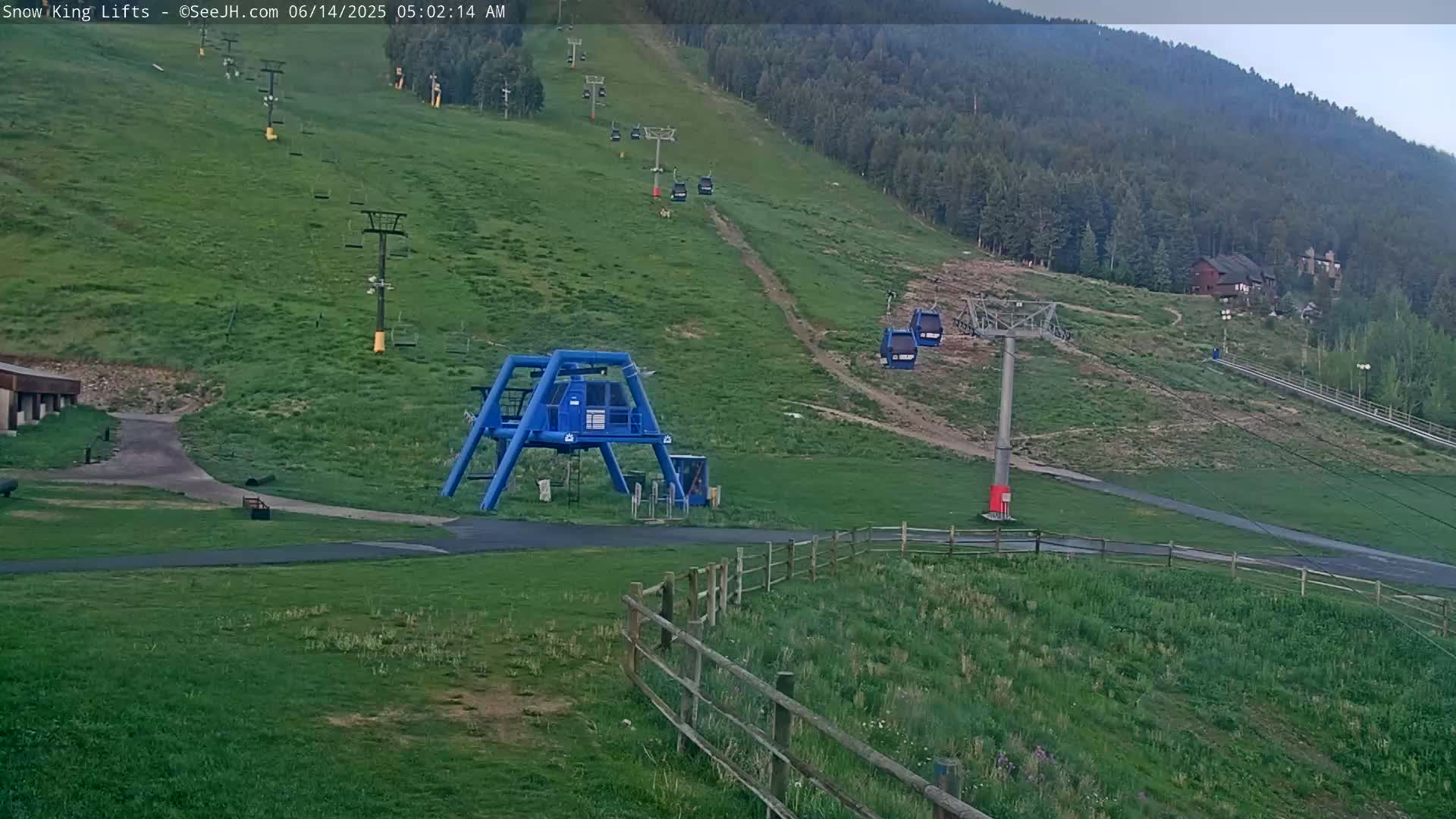 A grassy hillside with several empty chairlifts and a blue gondola station is visible under overcast skies.