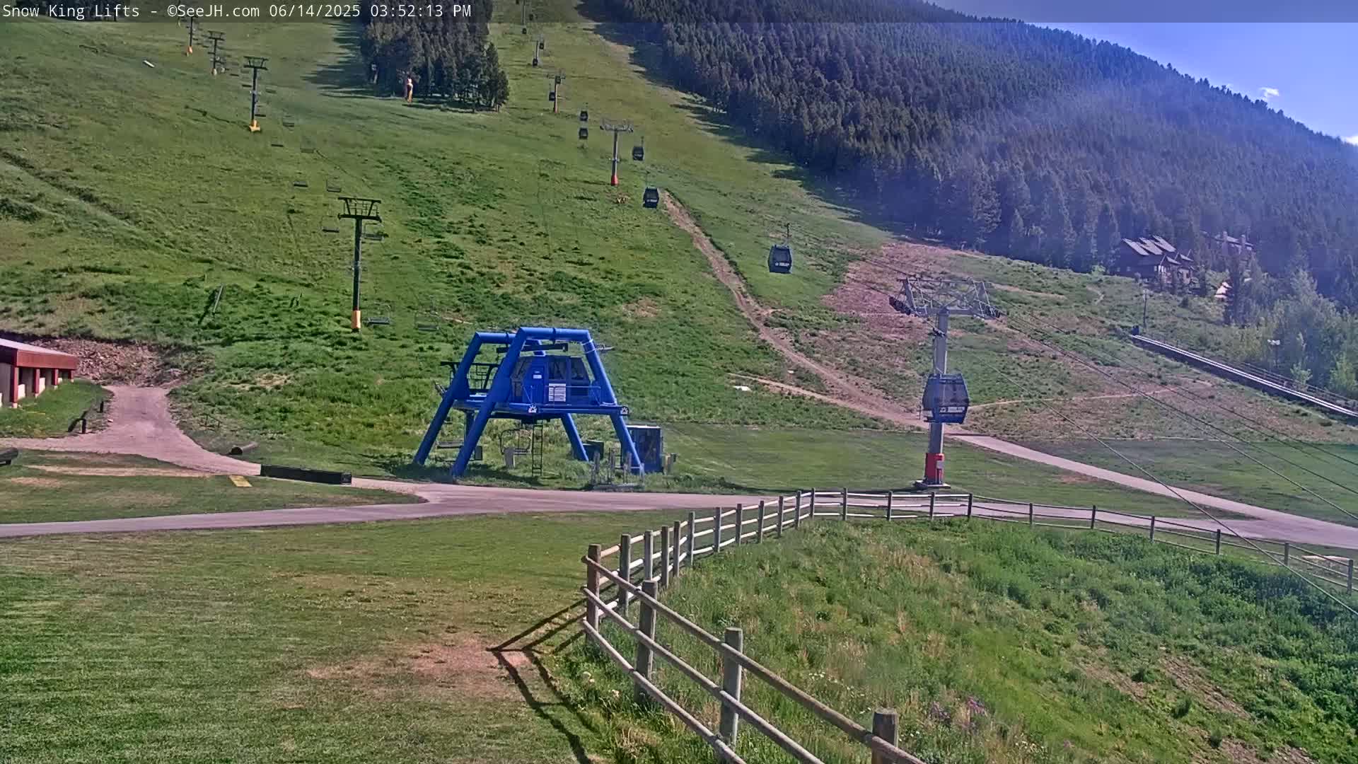 A white truck is parked near a ski lift base at the bottom of a grassy hill dotted with several chairlifts ascending a mountainside under a partly sunny sky.