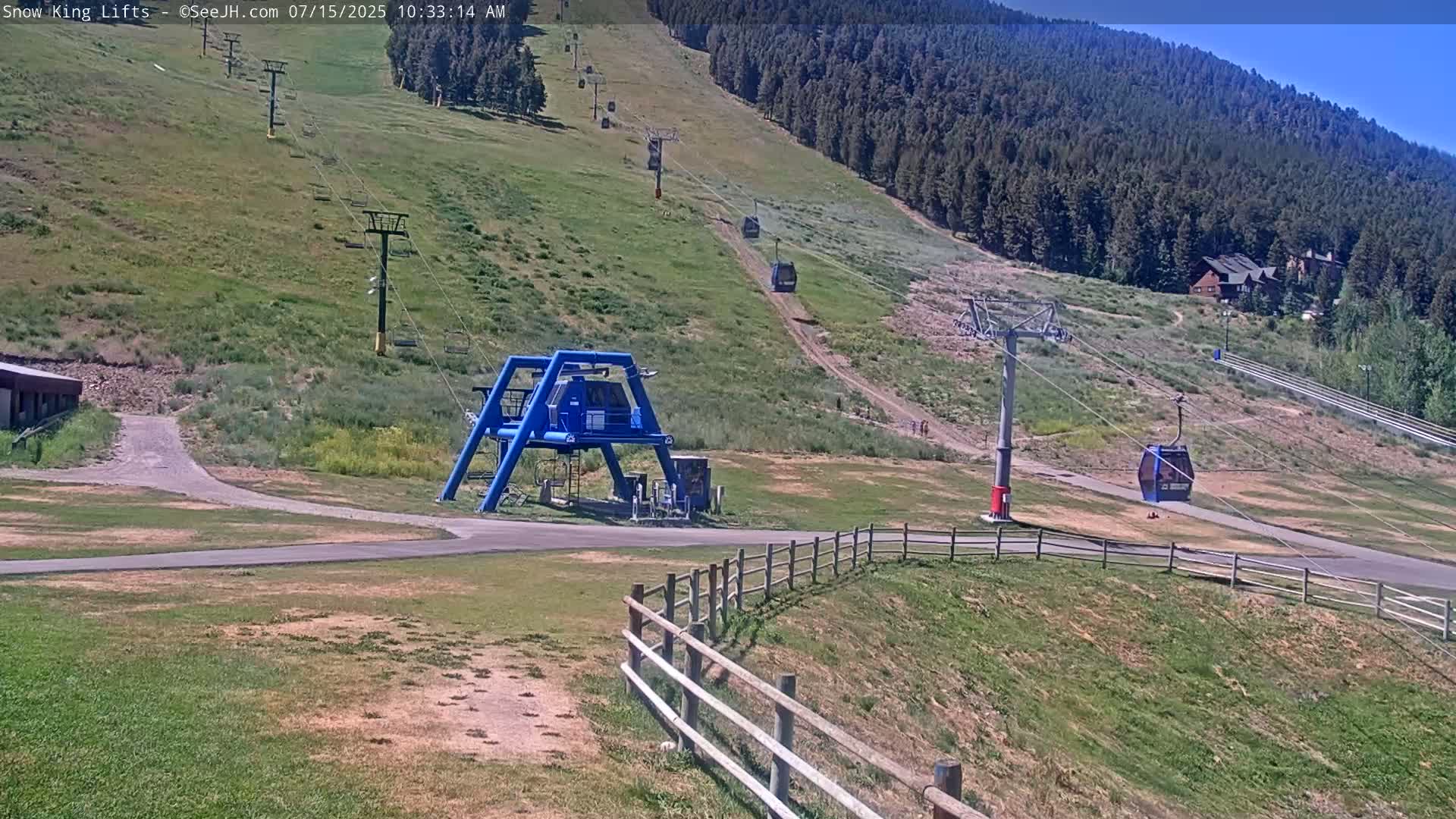 A ski lift base station with several chairlifts ascending a grassy hill under a clear, sunny sky.