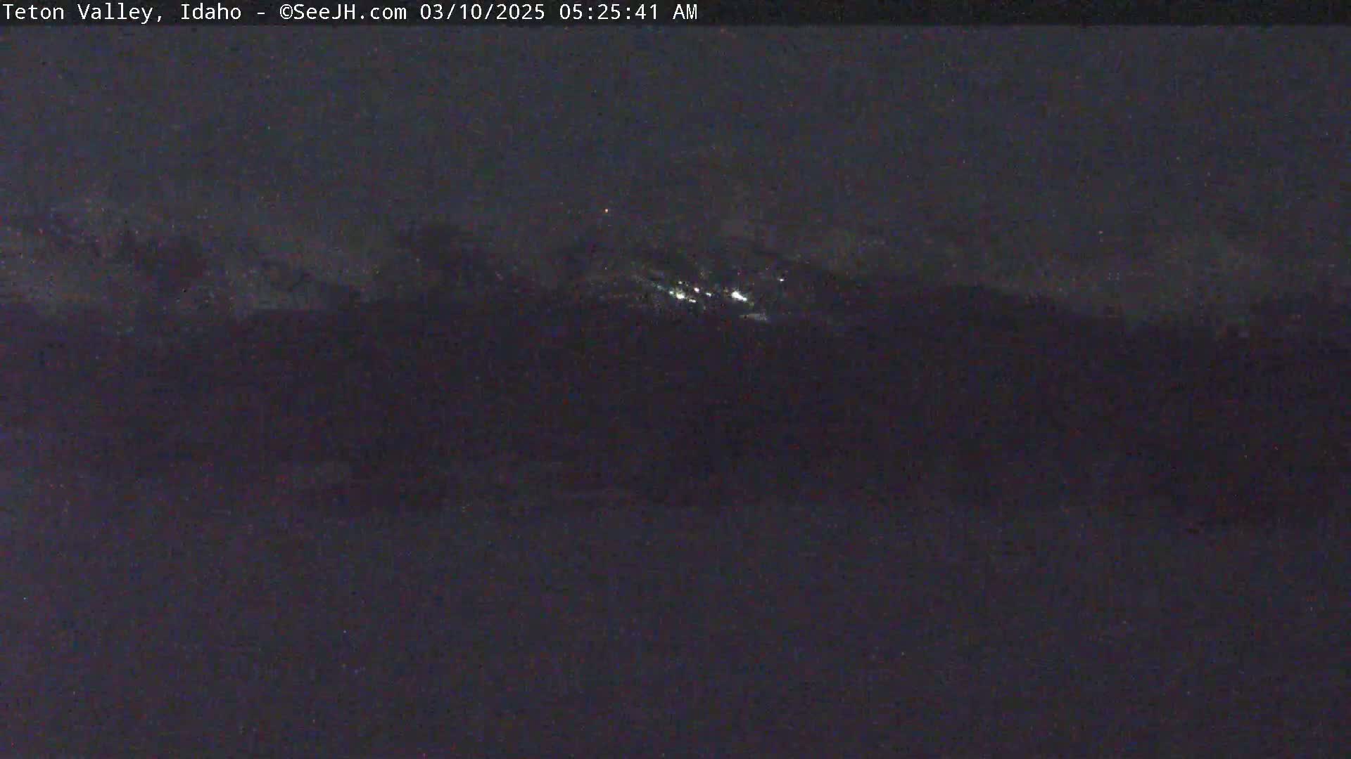 A nighttime, long shot of dimly lit mountains under a dark sky.