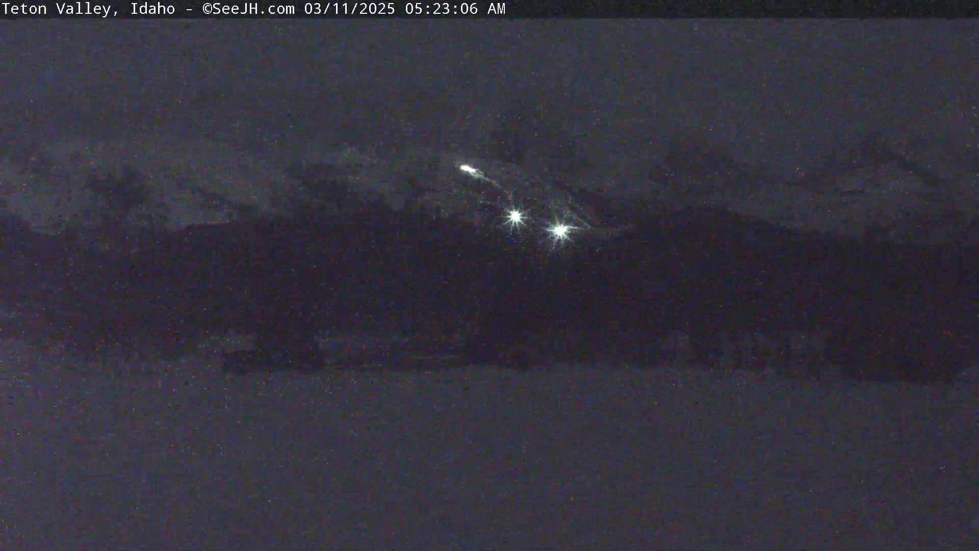 A nighttime, snowy landscape is shown with a few bright lights visible in the distance.
