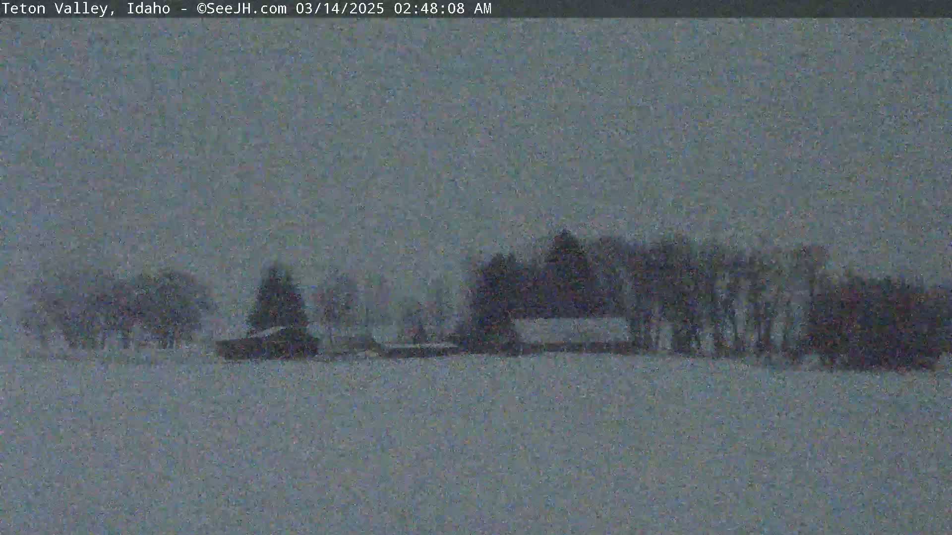 A snow-covered landscape with a few dark buildings and trees is visible under an overcast sky.