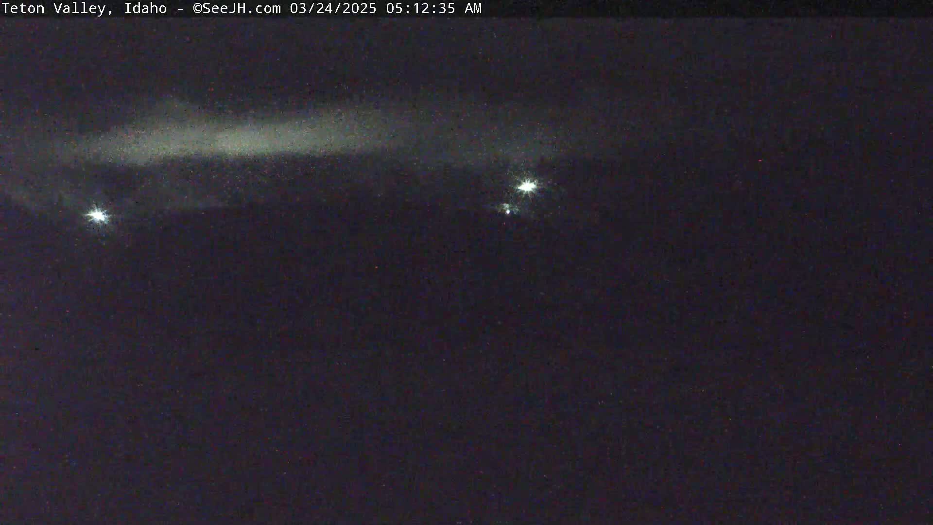 A nighttime, dark sky shows a faint, horizontally-oriented cloud formation and two bright lights.