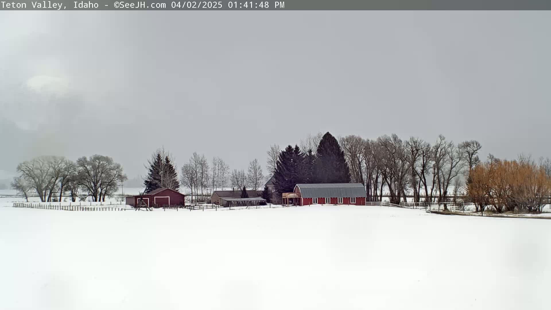 A snow-covered farmstead with a red barn and other outbuildings is visible under a cloudy, overcast sky.