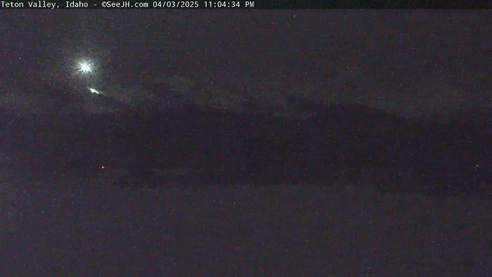 A nighttime long shot shows a bright moon and some faint clouds above dark mountains under a mostly clear sky.