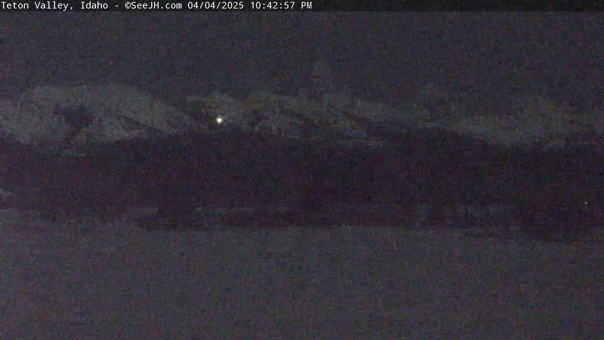 A nighttime view of snow-covered mountains under a dark, possibly cloudy sky.